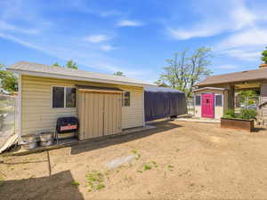 Expansive outdoor space featuring a detached storage shed with a vibrant magenta door, an additional utility shed, and a covered structure