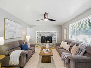 Living space featuring a brick fireplace with a painted finish, wood-finish flooring, a ceiling fan, and a large window with blinds