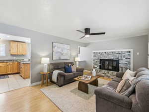 Living area featuring a brick-surround fireplace, light wood-finish flooring, and a ceiling fan