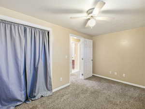 Carpeted room featuring a ceiling fan with light fixture, neutral wall paint, white baseboards, and a white paneled door