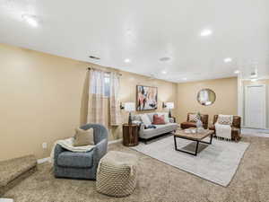 Spacious carpeted room featuring recessed lighting, a white paneled door, and a single window with vertical blinds