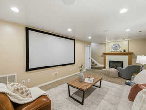 Built-in projection screen with recessed lighting, carpeted flooring, white baseboards, and a fireplace with a wood mantle