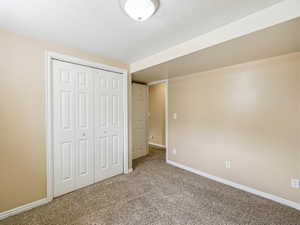 Carpeted room featuring a white bi-fold closet, neutral-toned walls, white baseboards, and a flush-mount ceiling light fixture