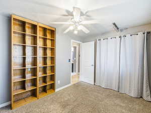 Built-in shelving units with wood-finish, ceiling fan with integrated lighting, track lighting fixture, neutral-toned carpeting, and a white two-panel interior door