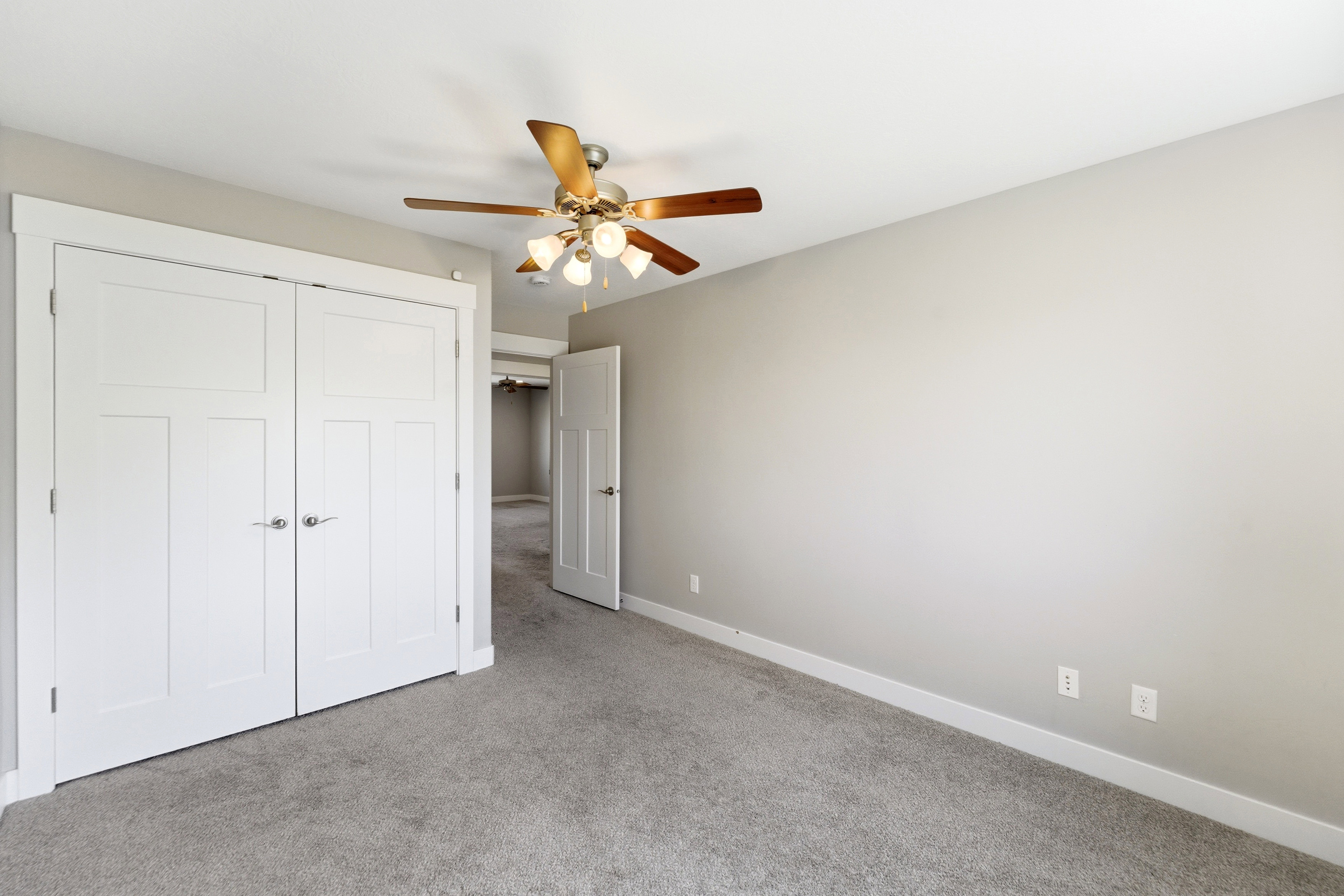 Neutral-toned room with light gray carpet, white baseboards, and a ceiling fan with wood-finish blades