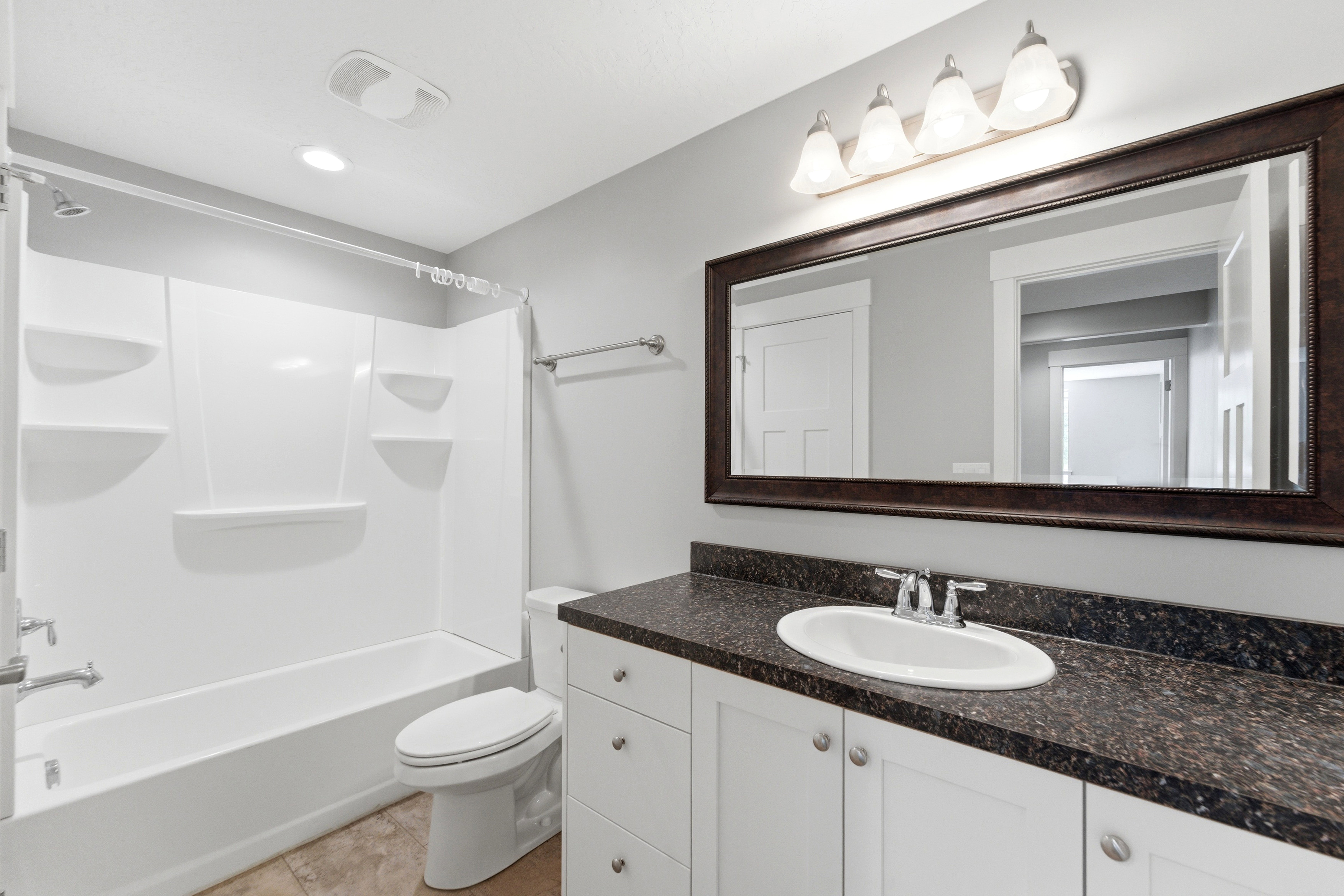 Bathroom featuring a white tub/shower combination, dark speckled countertop, white vanity cabinetry, a framed vanity mirror, and recessed lighting