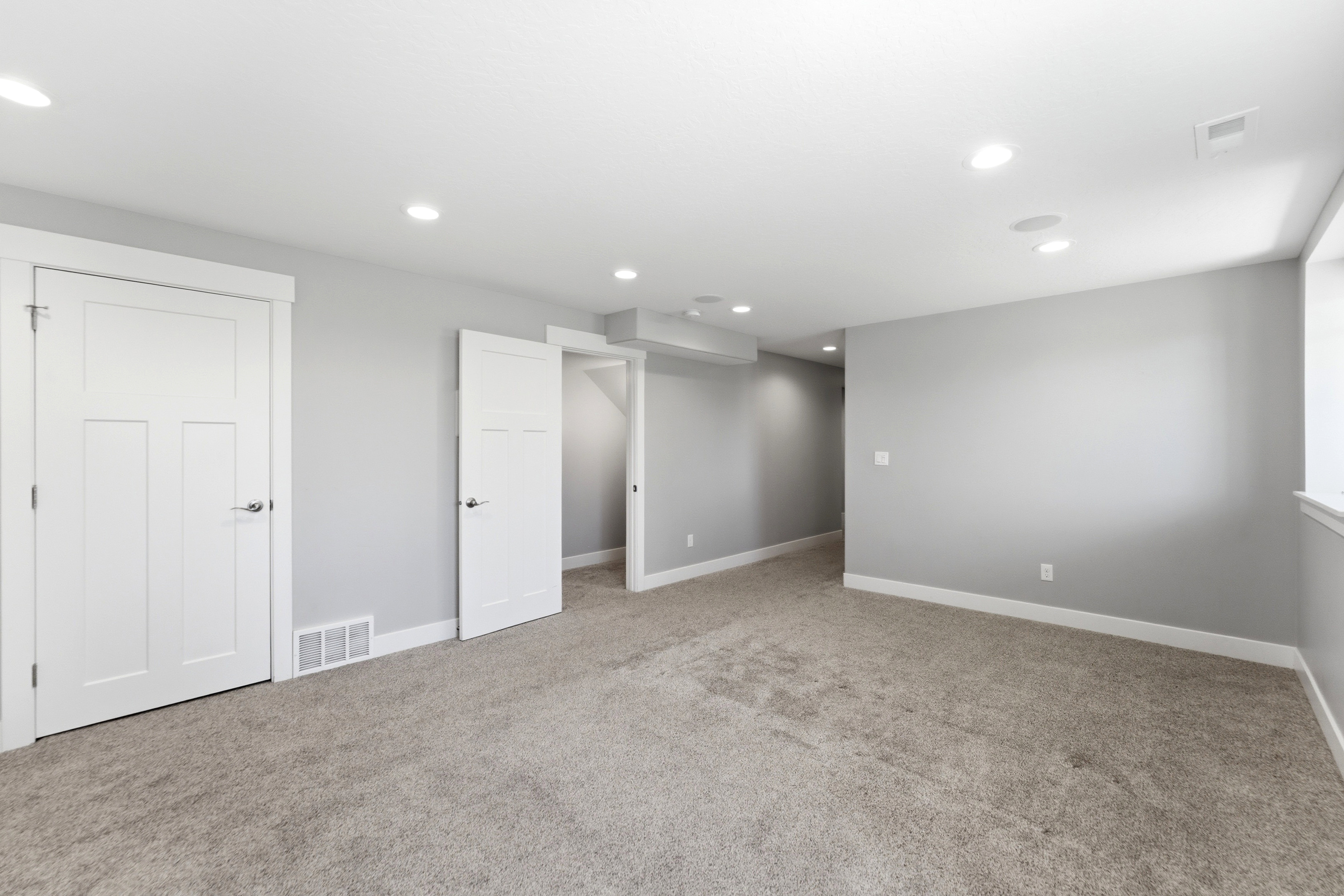 Spacious room featuring neutral gray walls, light-colored carpeting, white trim, and recessed lighting