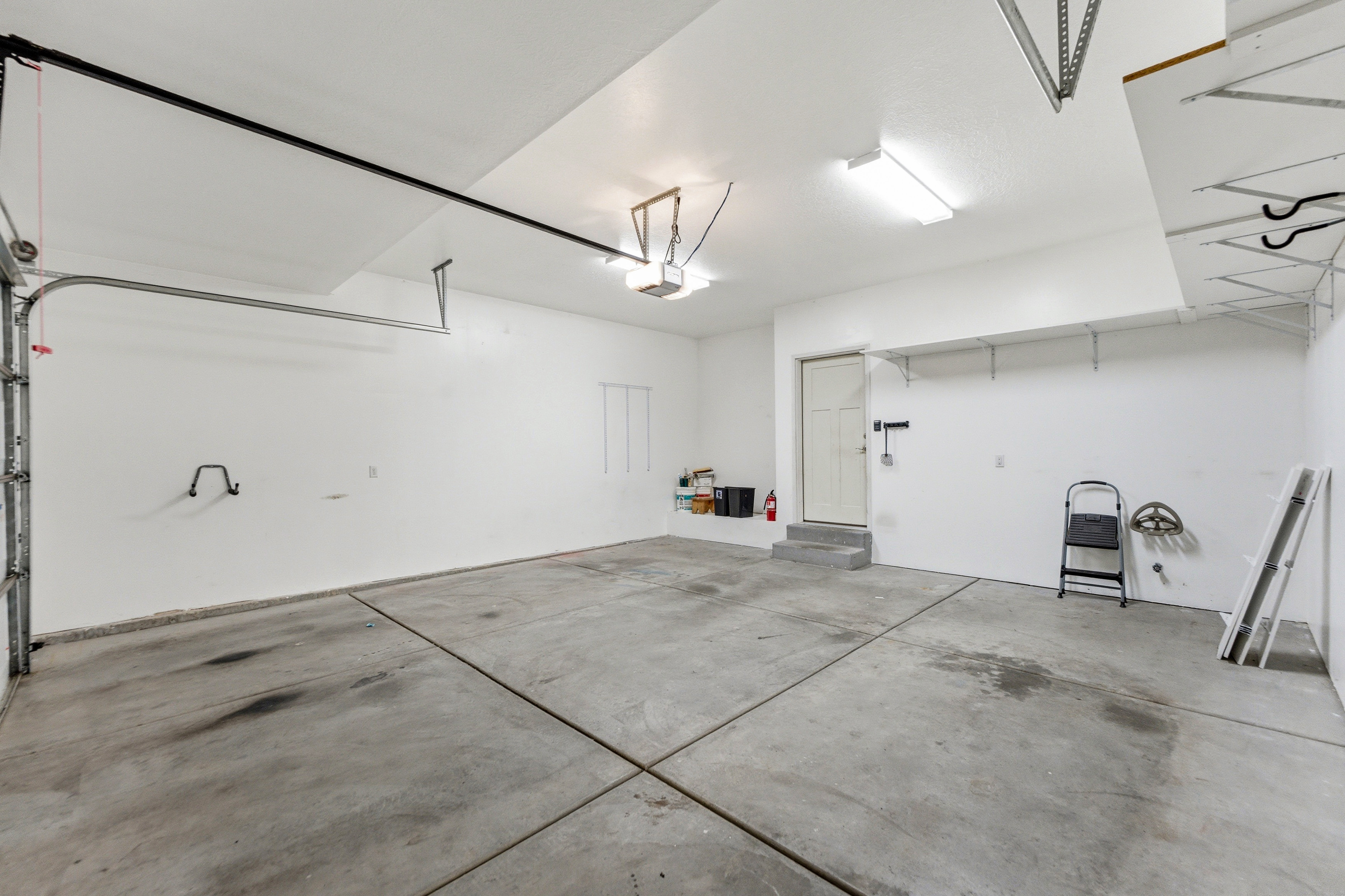 Spacious garage featuring a concrete floor, bright overhead lighting, a service door, and integrated shelving