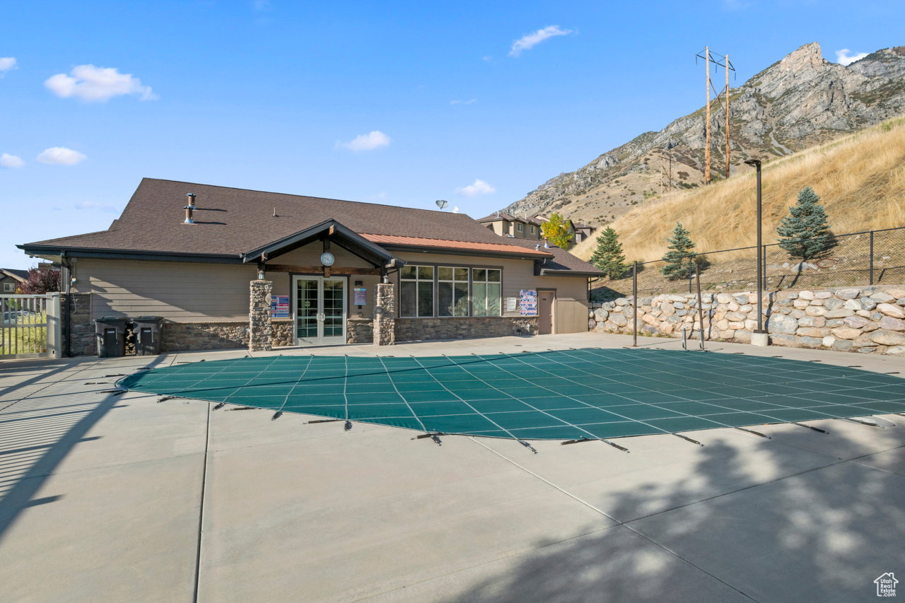 Community pool area featuring a covered pool, concrete decking, and an adjacent clubhouse with stone and siding exterior