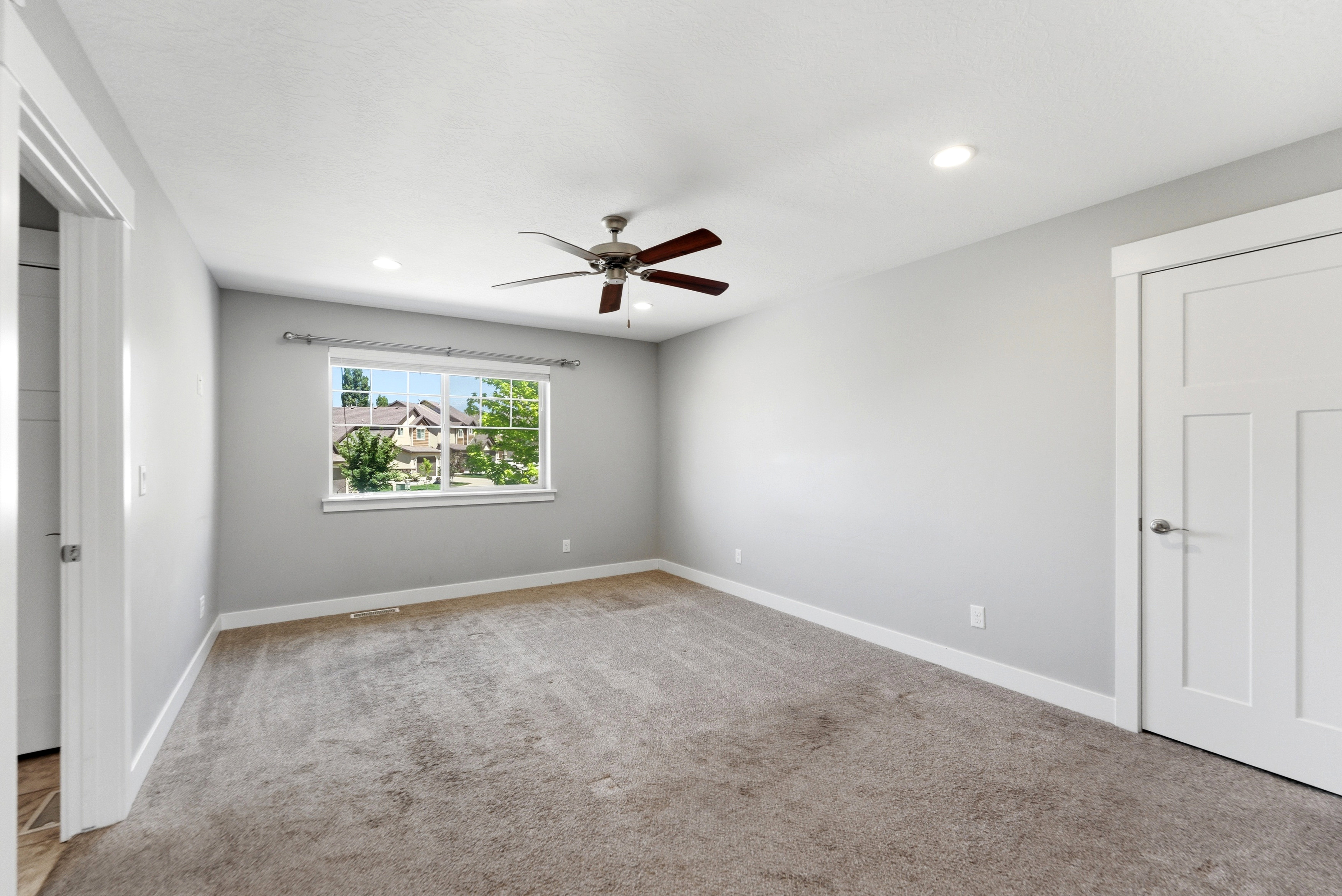 Spacious room featuring neutral carpeting, light gray walls, a window with white trim, recessed lighting, and a ceiling fan