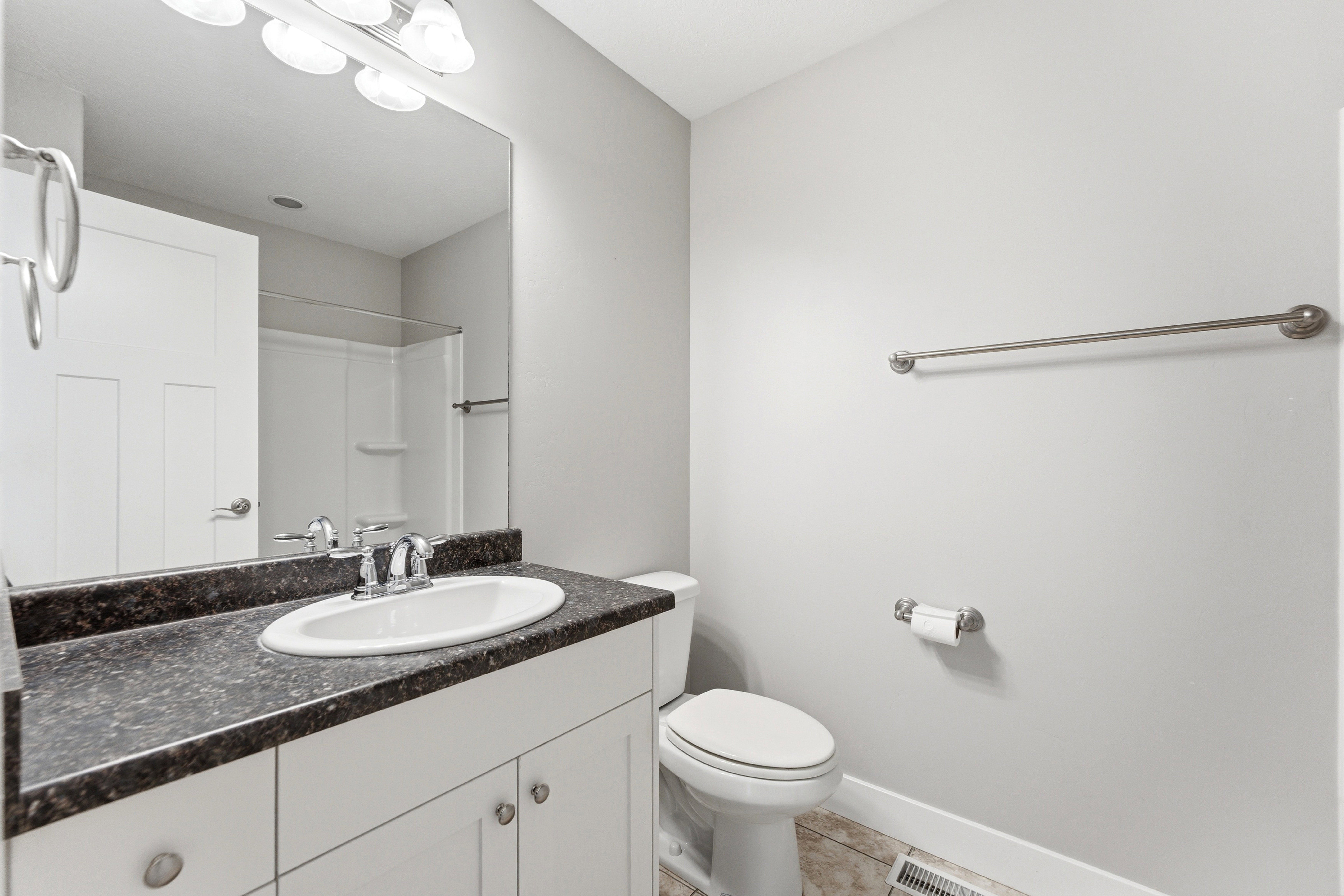 Bathroom featuring a white vanity with double-door cabinetry, a speckled dark countertop, and a built-in oval sink with a chrome faucet