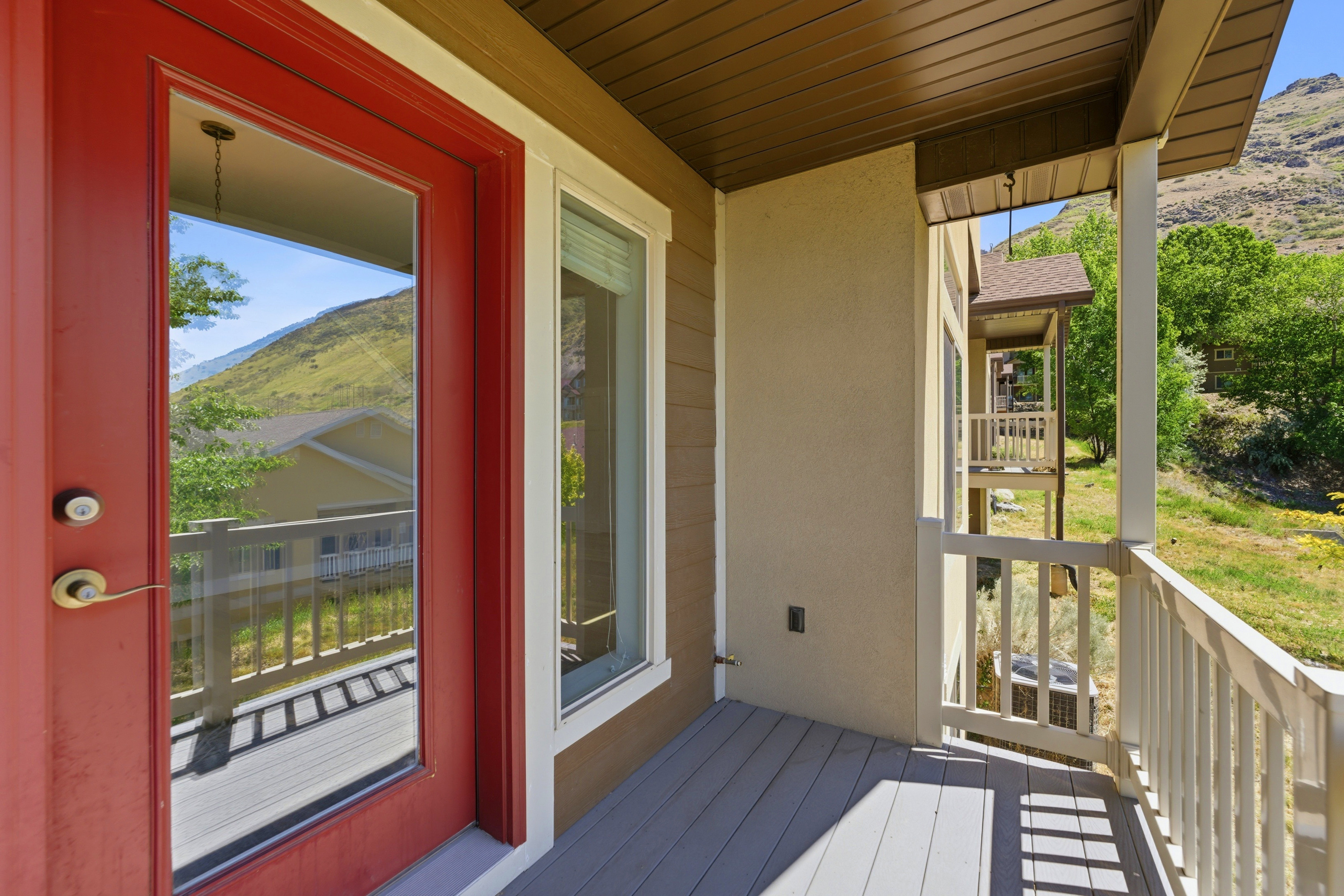 Exterior porch area featuring a red glass-paneled door, a white-trimmed window, composite decking, and white railing