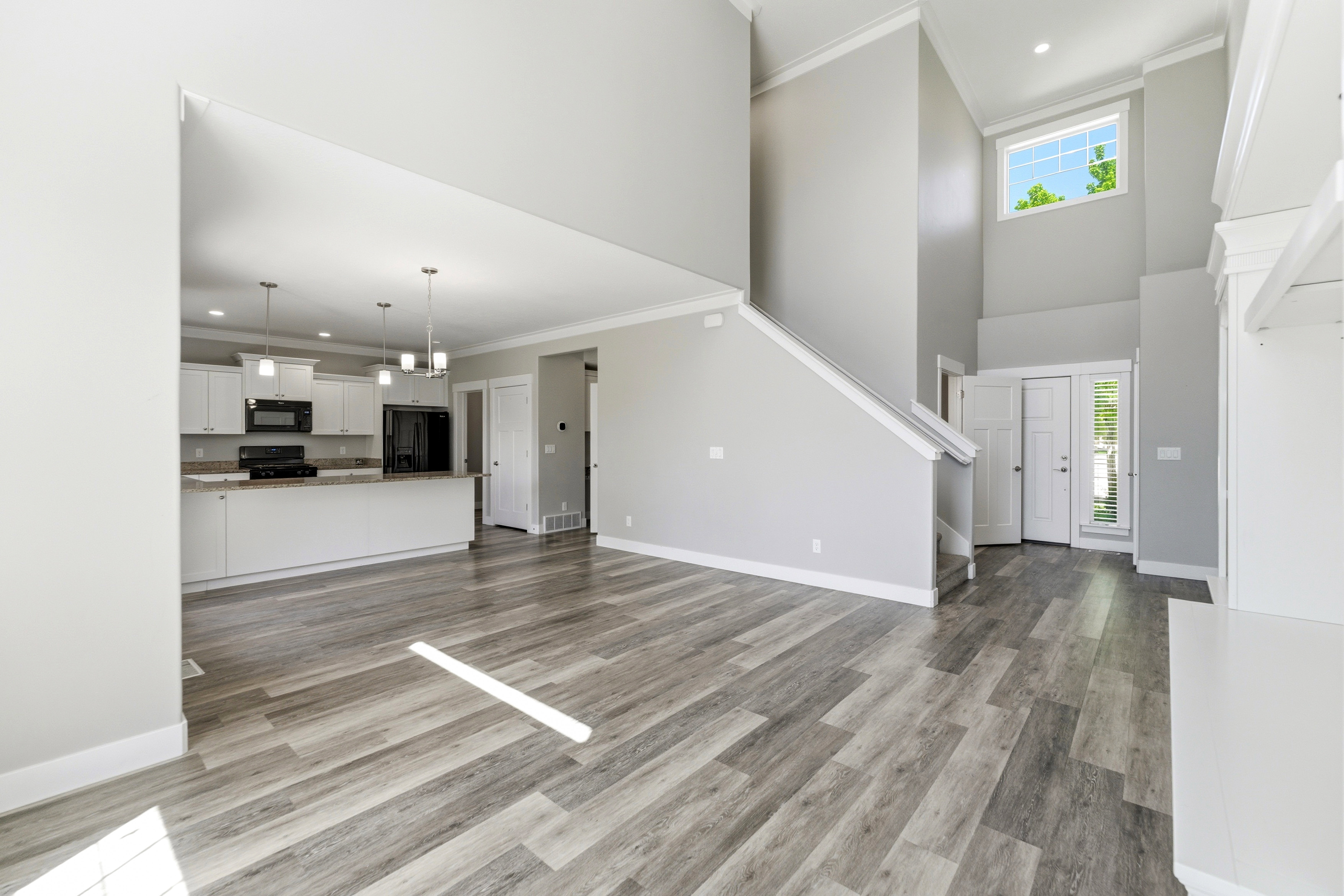 Open-concept living space featuring wood-finish flooring, a two-story foyer with a transom window, white kitchen cabinetry with a contrasting countertop, and a built-in shelving unit
