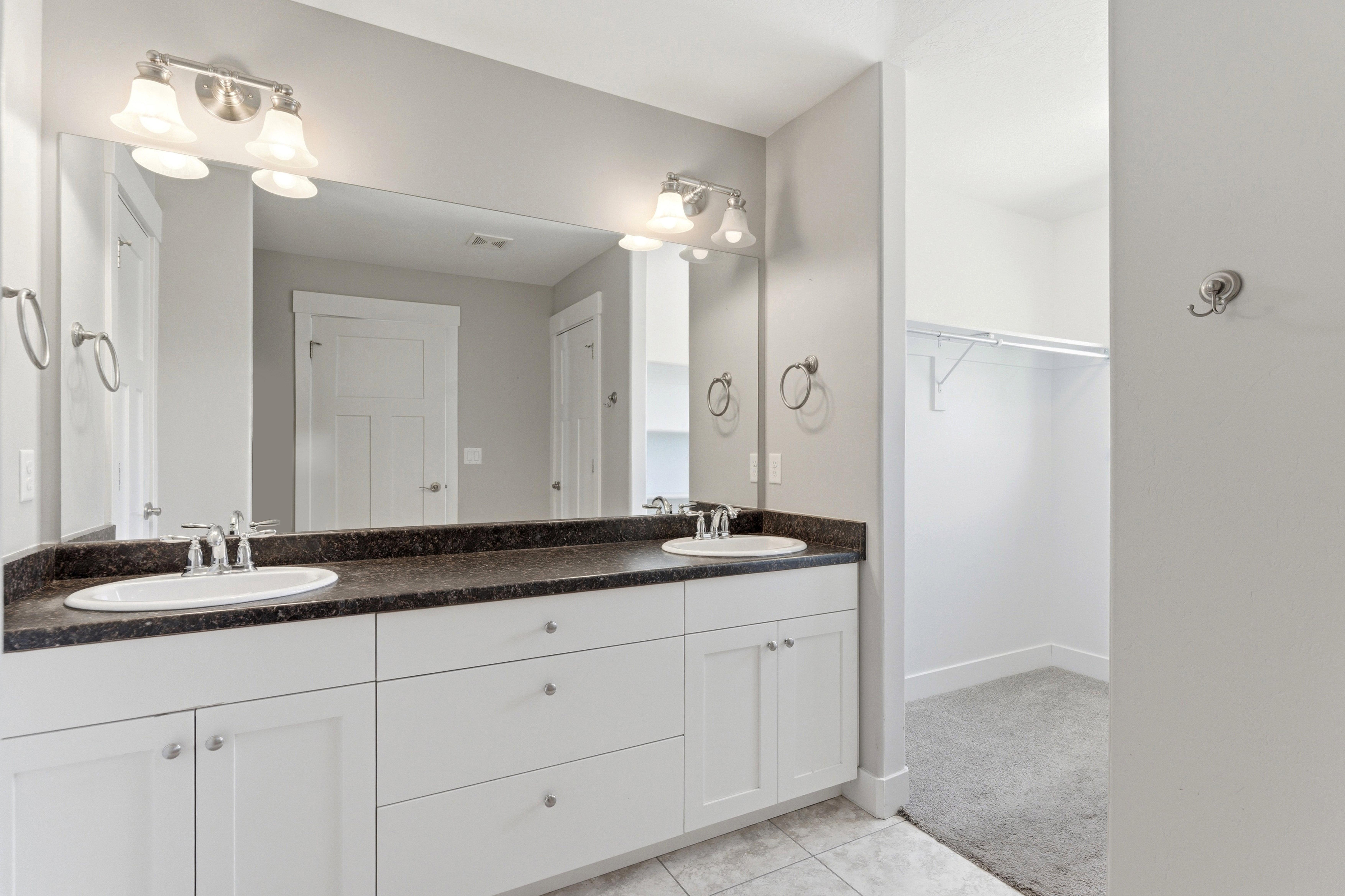 Double vanity with white cabinetry, dark countertop, dual undermount sinks, and chrome faucets