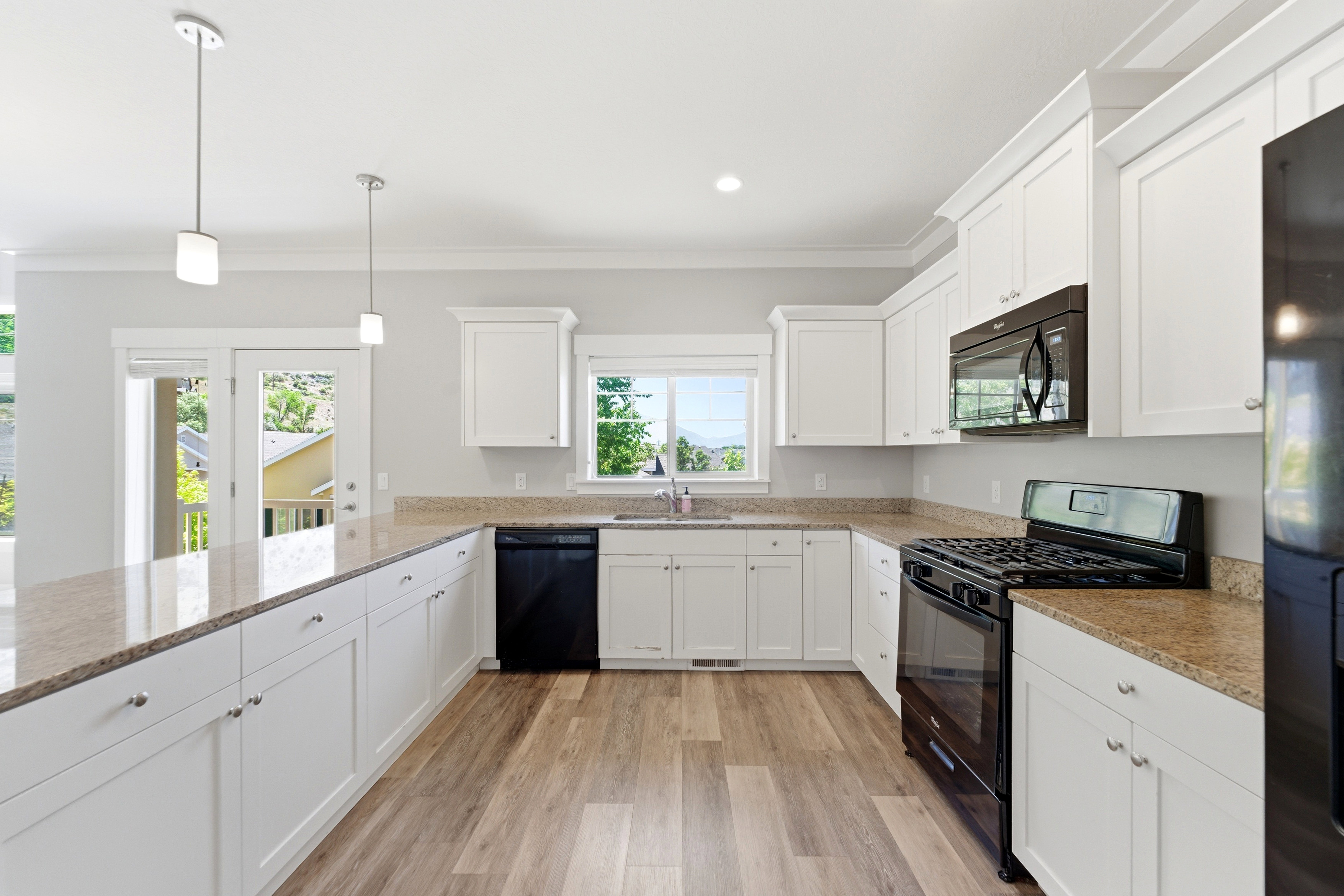 Bright kitchen featuring white shaker cabinetry, stone-look countertops, and stainless steel appliances