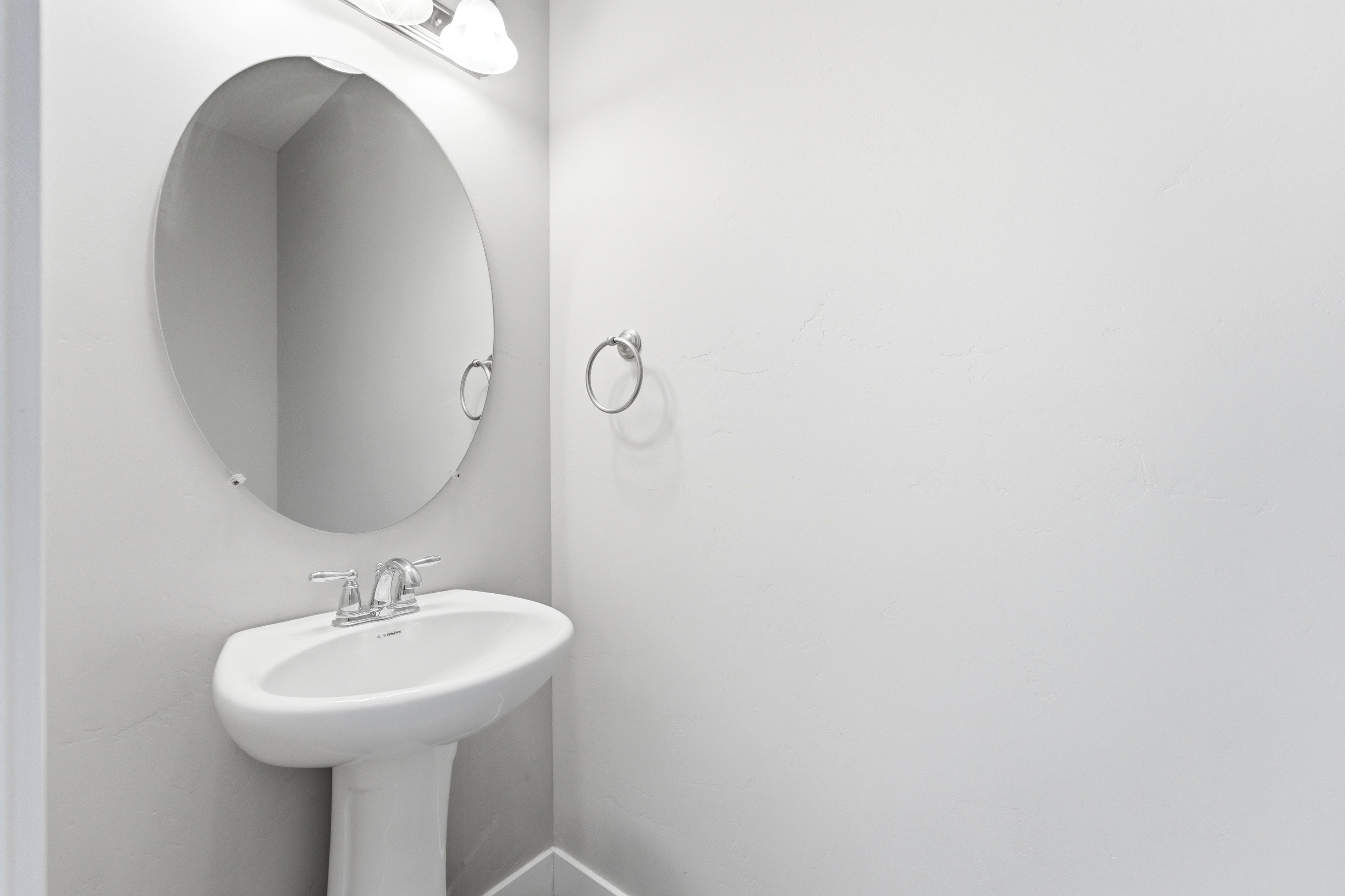 Pedestal sink with chrome faucet, complemented by an oval wall-mounted mirror