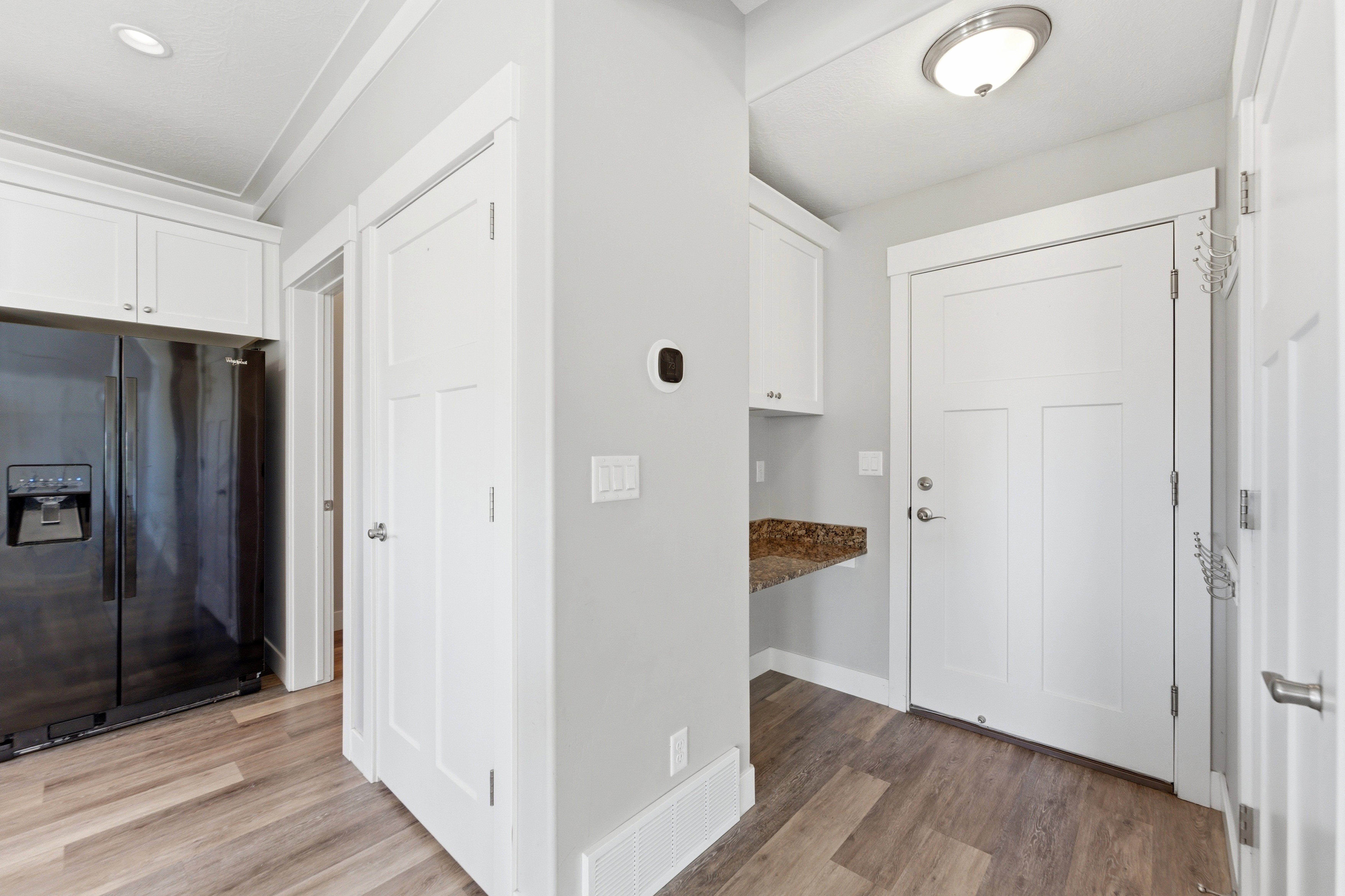 Utility area featuring a built-in granite-look countertop, white cabinetry, wood-finish flooring, and white paneled doors