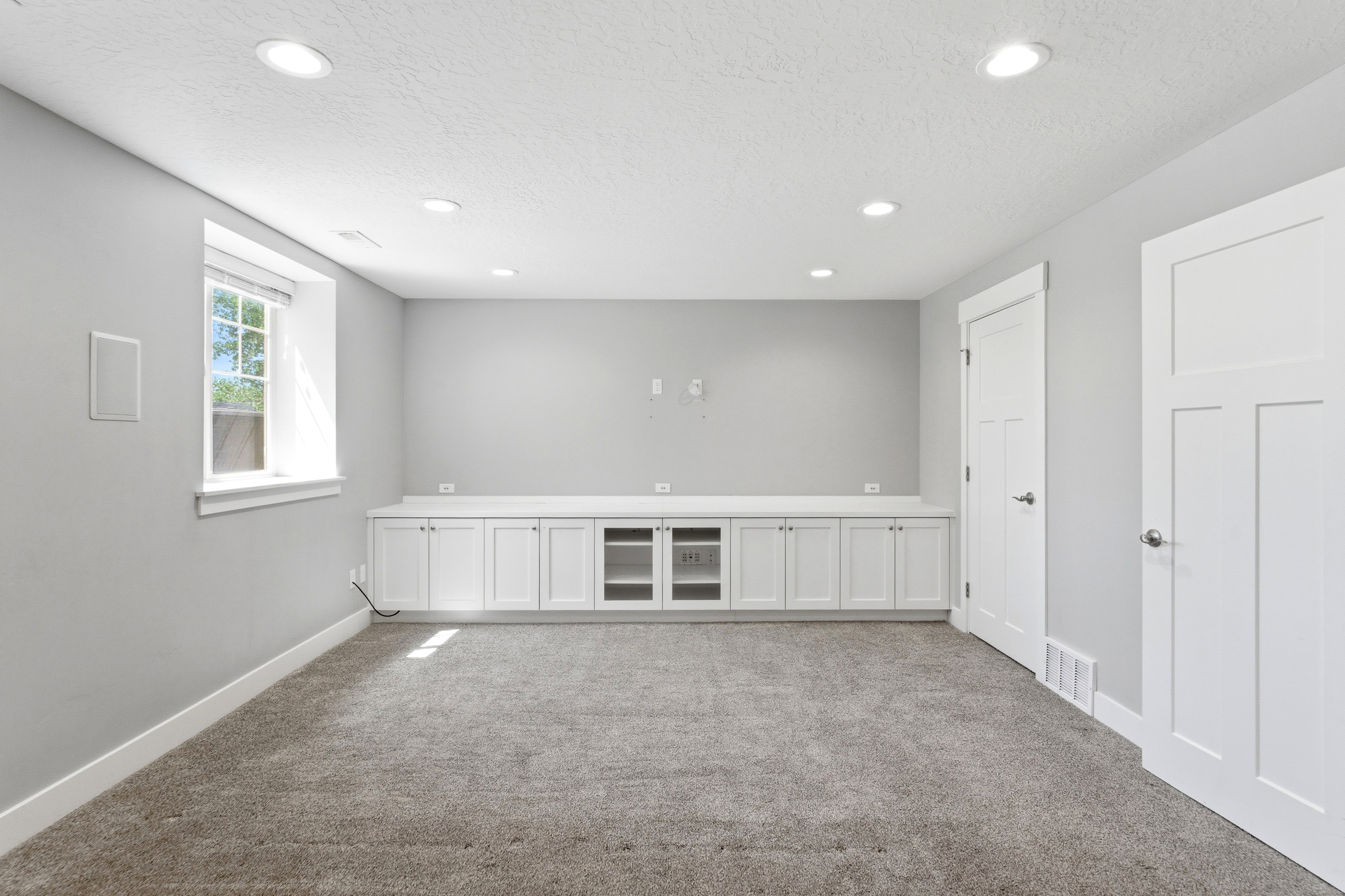 Spacious room featuring extensive built-in cabinetry with a countertop, recessed lighting, a single window, and neutral carpeting