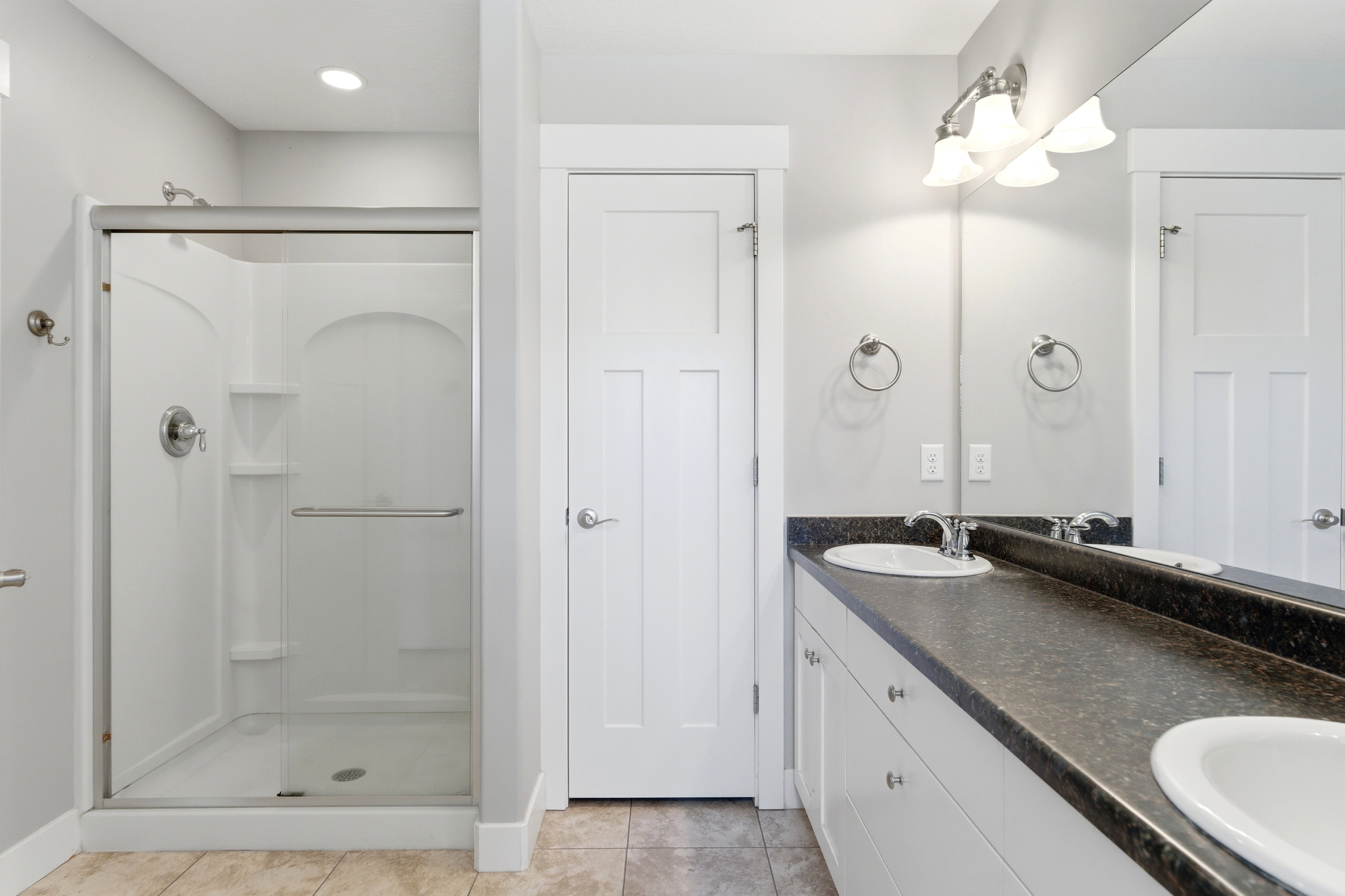 Bathroom featuring a glass-enclosed shower, dual vanity with undermount sinks, and a dark countertop