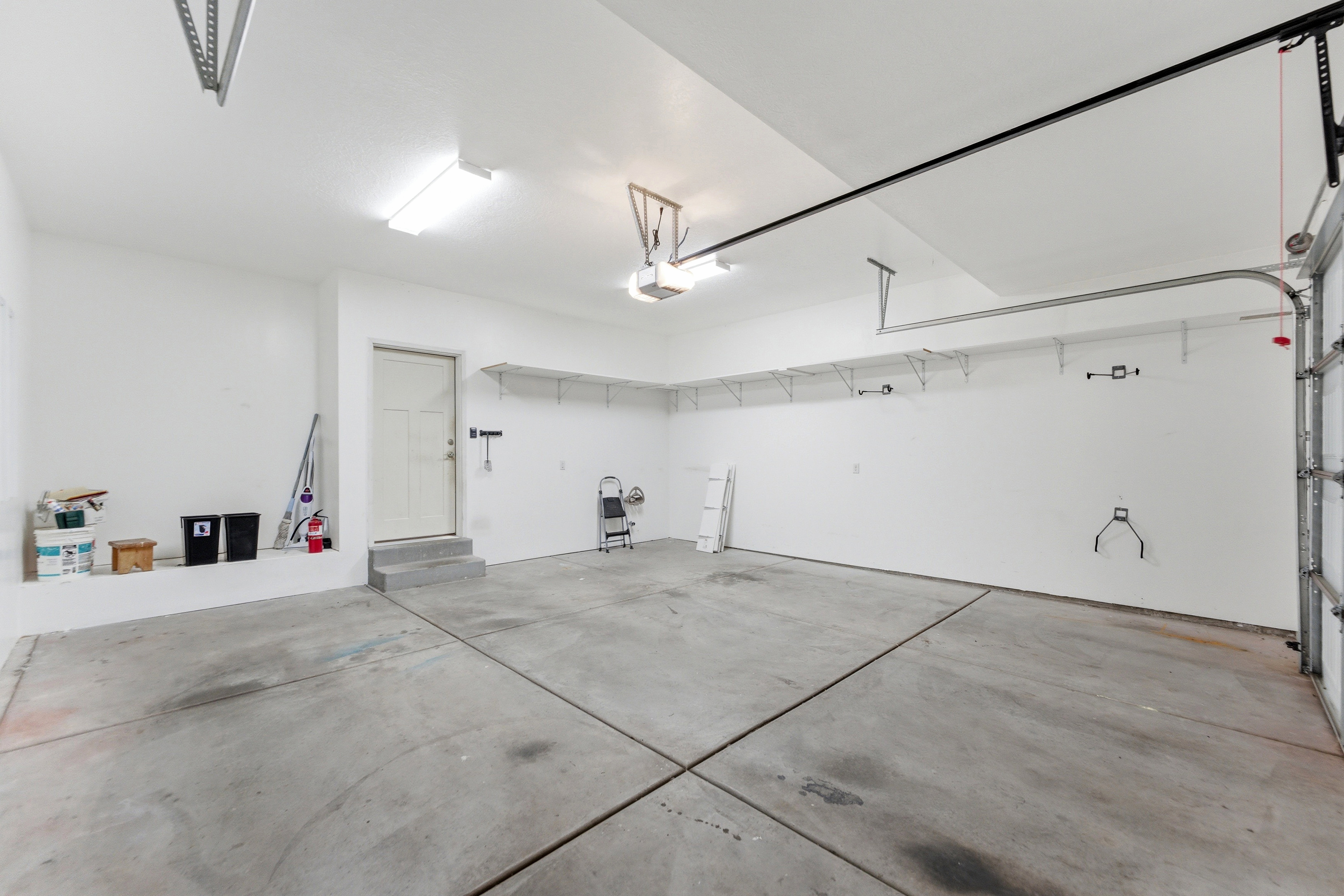 Spacious garage featuring concrete flooring, ample overhead lighting, built-in wall shelving, an overhead garage door, and an interior access door
