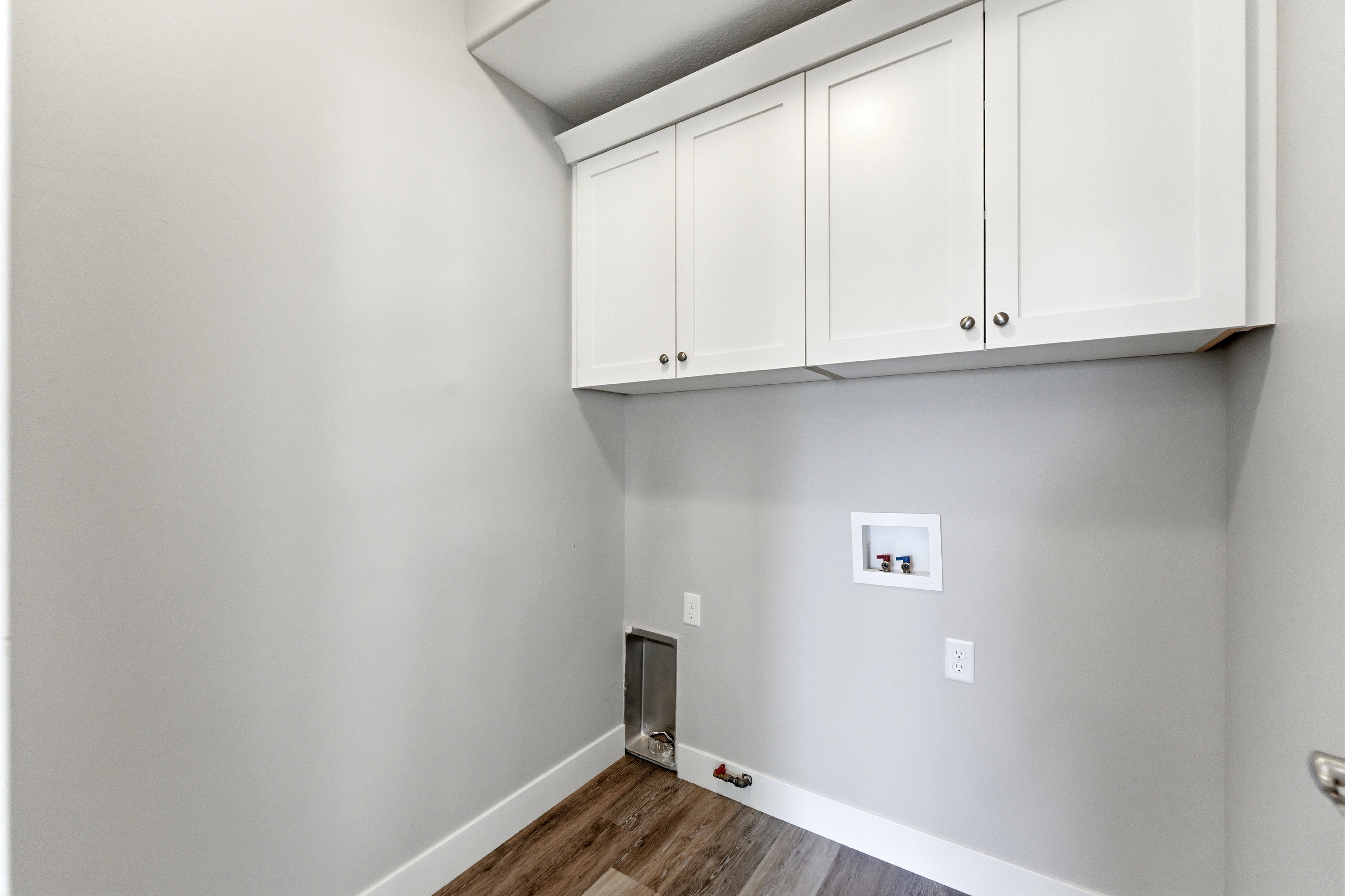 Utility area featuring overhead white shaker cabinetry, wood-finish flooring, and white baseboards