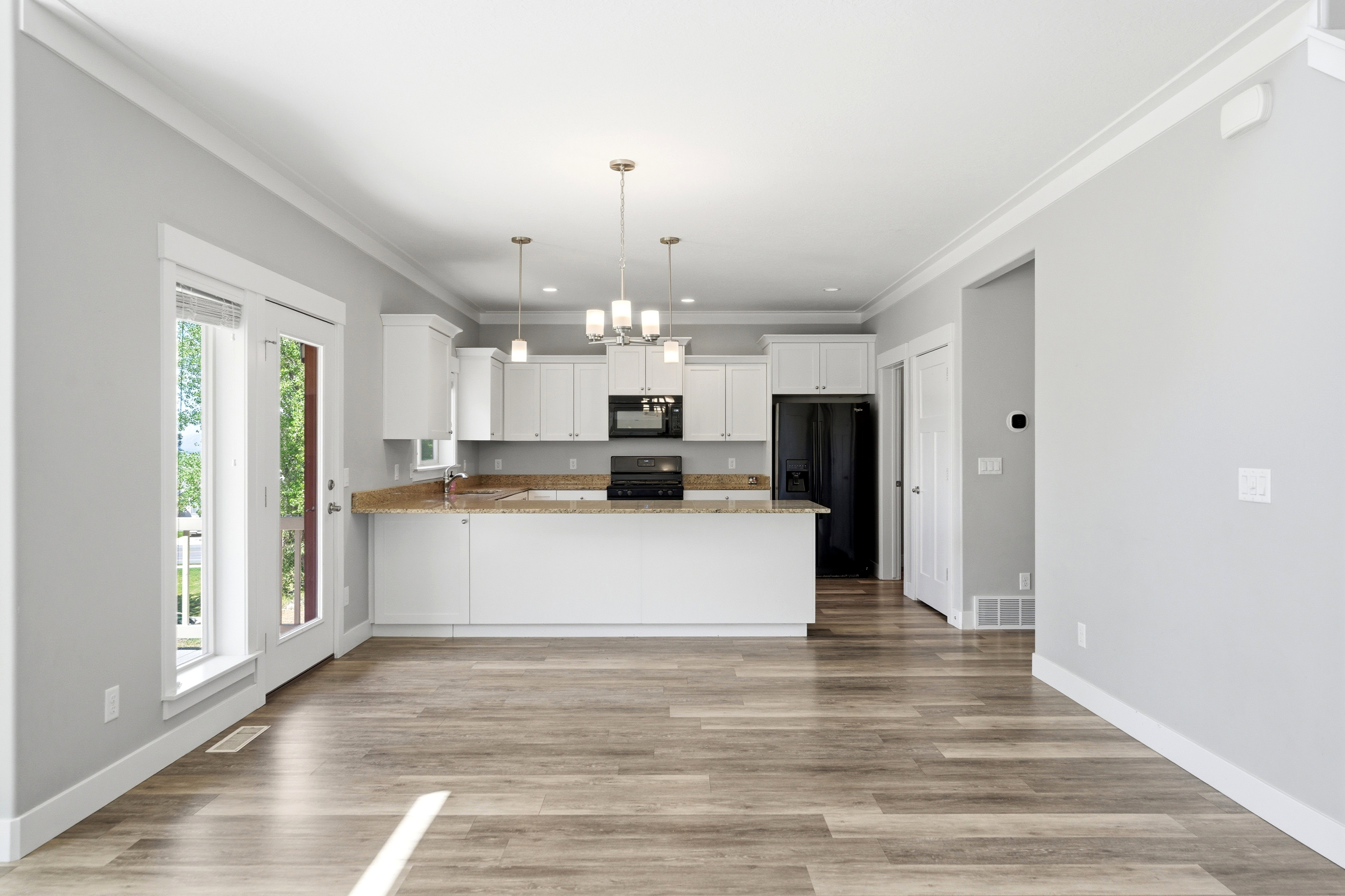 Open-concept living space with wood-finish flooring, white cabinetry, a built-in kitchen island with stone-finish countertops, pendant lighting, and double glass-paneled doors leading to an outdoor area