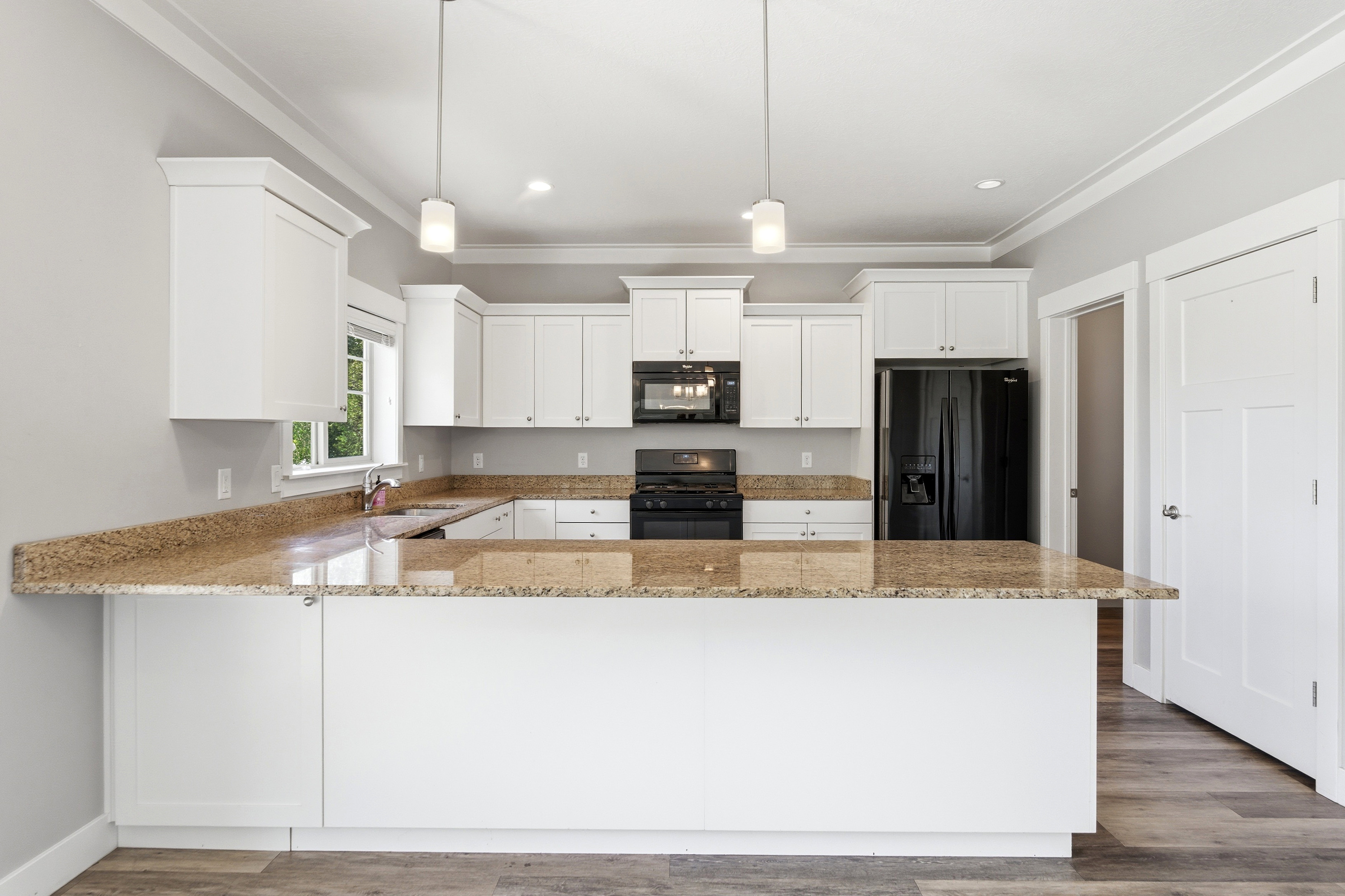 Kitchen featuring white cabinetry, speckled countertops, black appliances, a central island, and wood-finish flooring