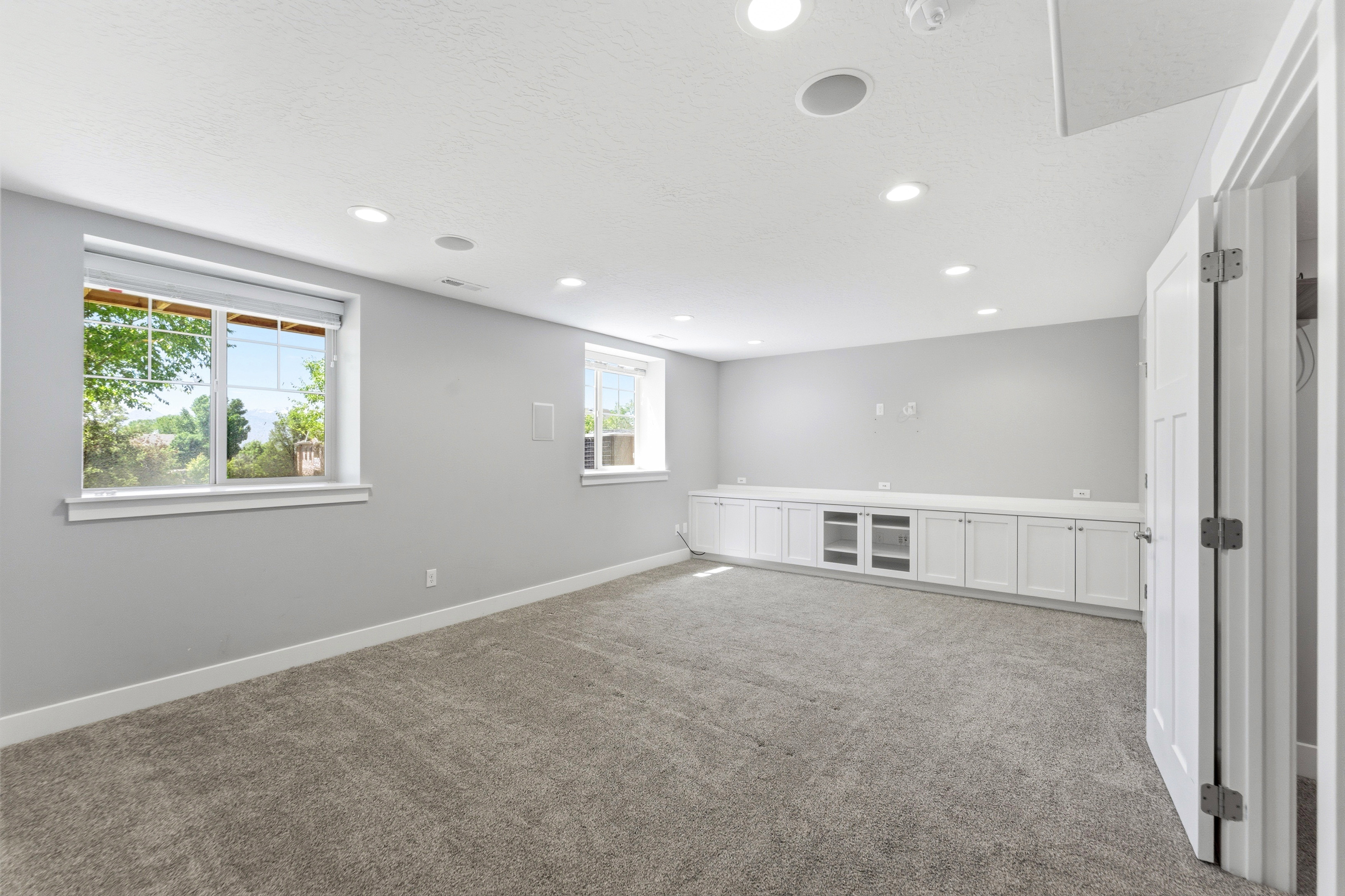 Spacious room featuring light gray walls, plush gray carpeting, and recessed lighting