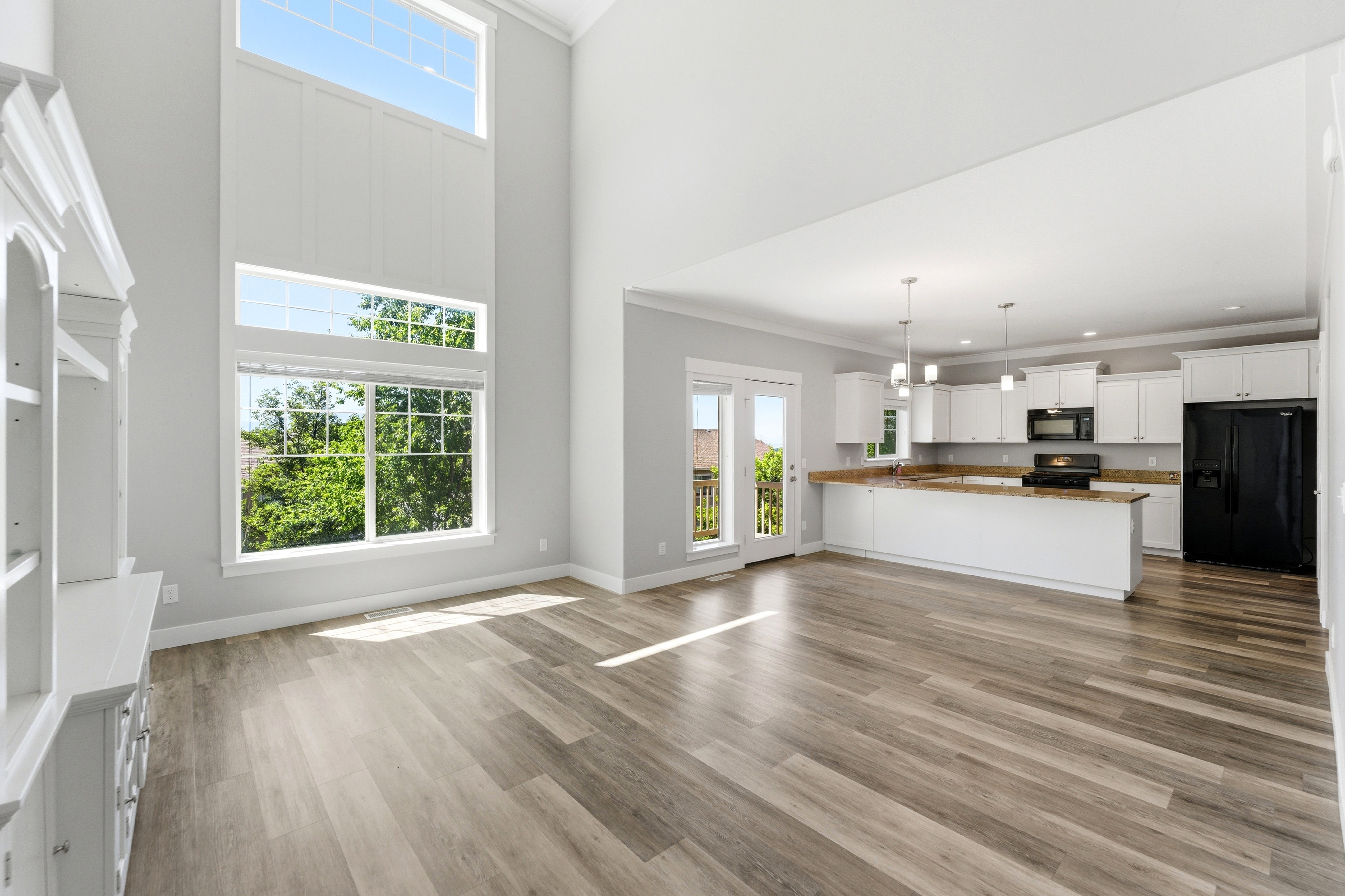 Great room featuring soaring ceilings, expansive windows, wood-finish flooring, a built-in display cabinet, and an open-concept kitchen with white cabinetry and stainless steel appliances