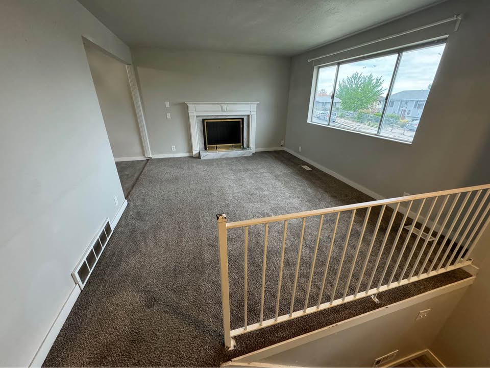 Unfurnished living room featuring dark colored carpet and a fireplace with raised hearth