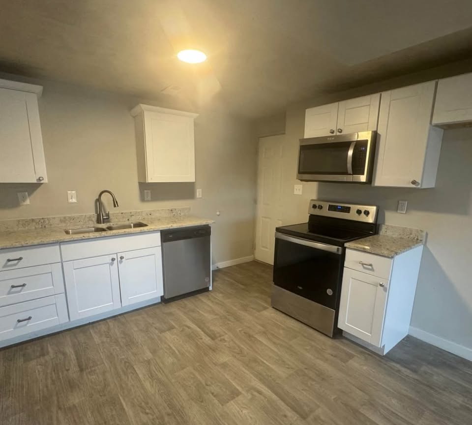 Kitchen with white cabinets, stainless steel appliances, light stone countertops, and light wood-style flooring