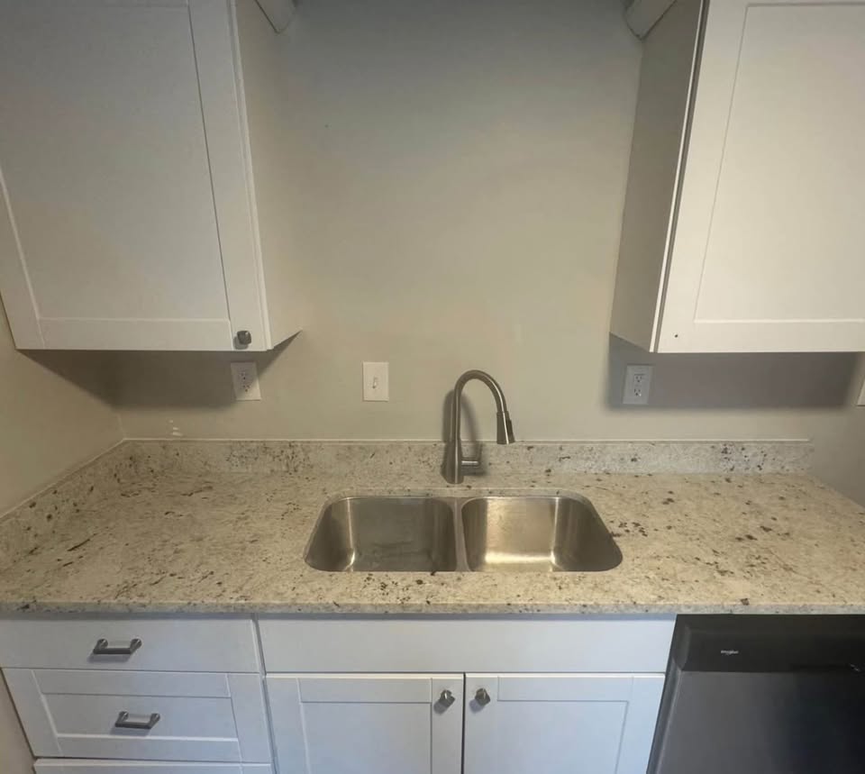 Kitchen featuring white cabinets, light stone counters, and dishwasher