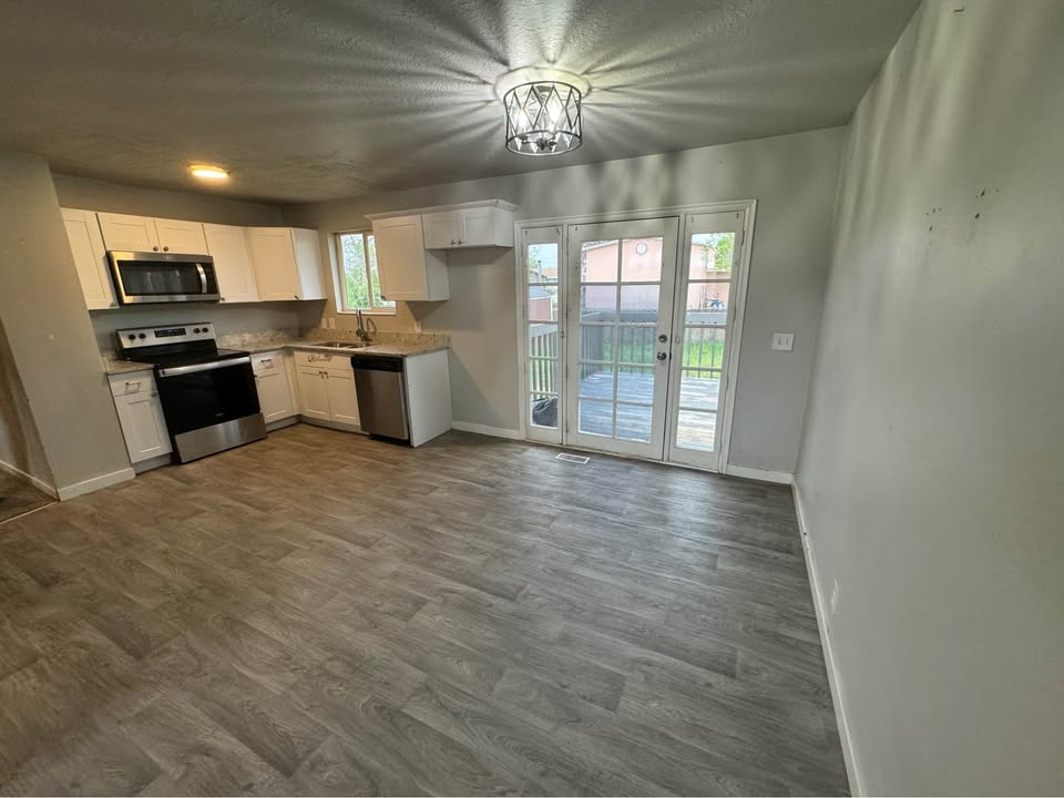 Kitchen featuring stainless steel appliances, white cabinets, and dark wood-style flooring