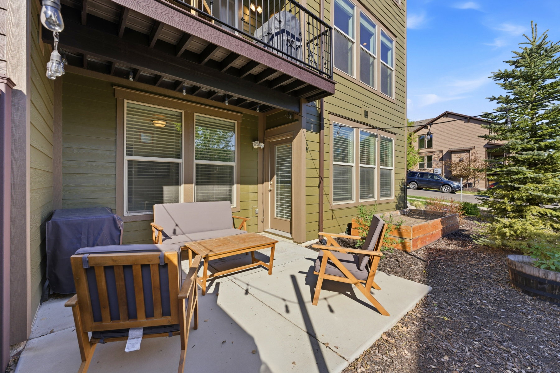 Private patio with concrete flooring, accented by an overhead balcony and string lighting