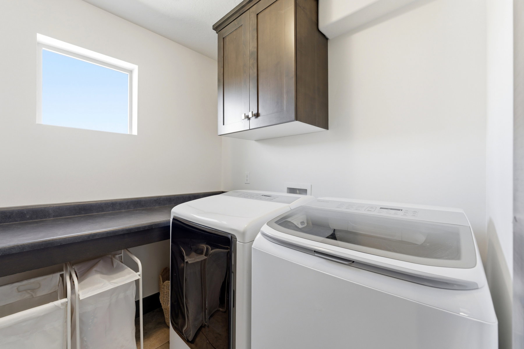 Dedicated laundry space featuring a built-in countertop, upper cabinetry with dark wood-finish doors, and a rectangular window