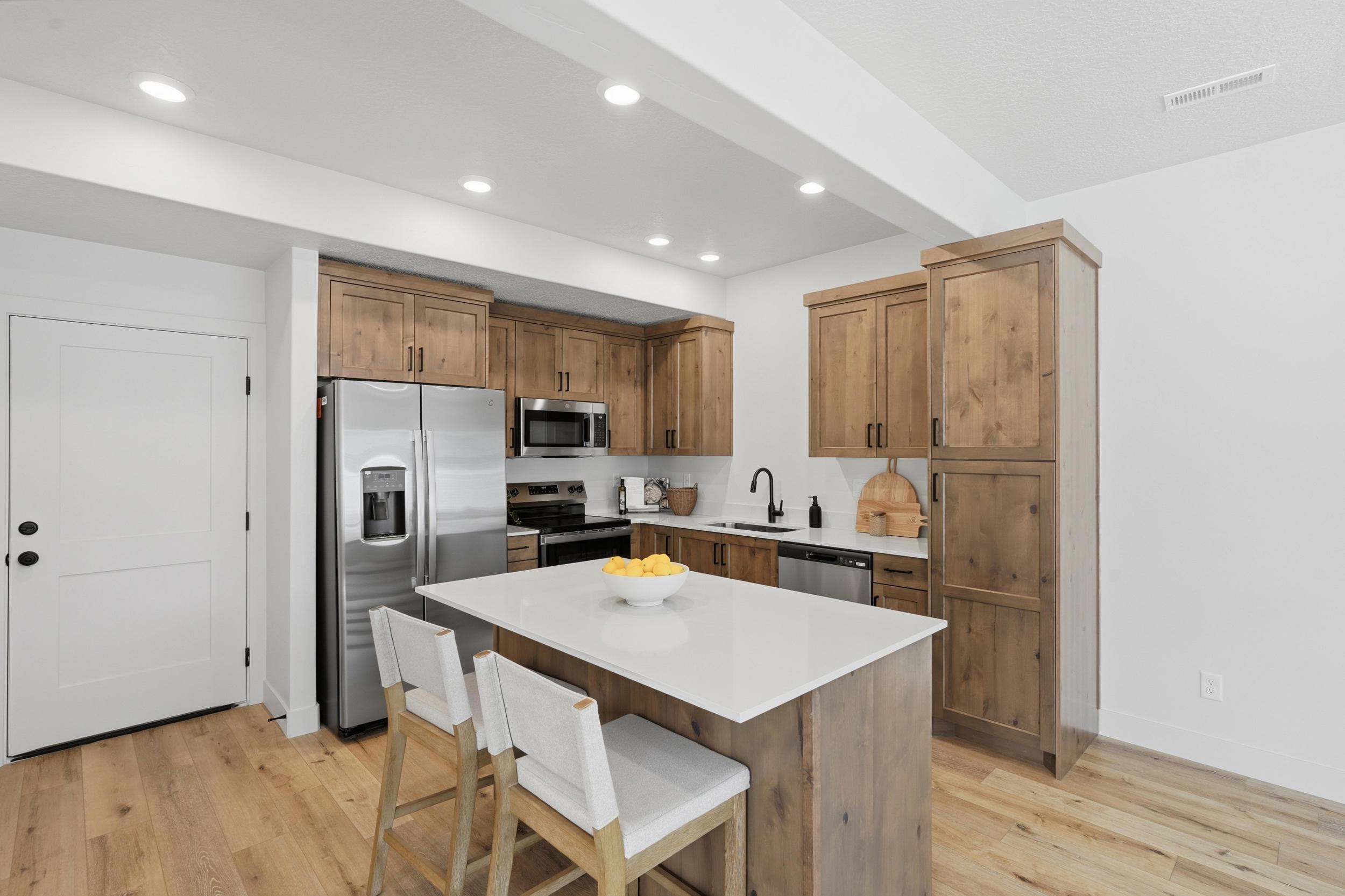 Contemporary kitchen featuring light wood-finish cabinetry and flooring, a white island countertop, stainless steel appliances, and recessed lighting