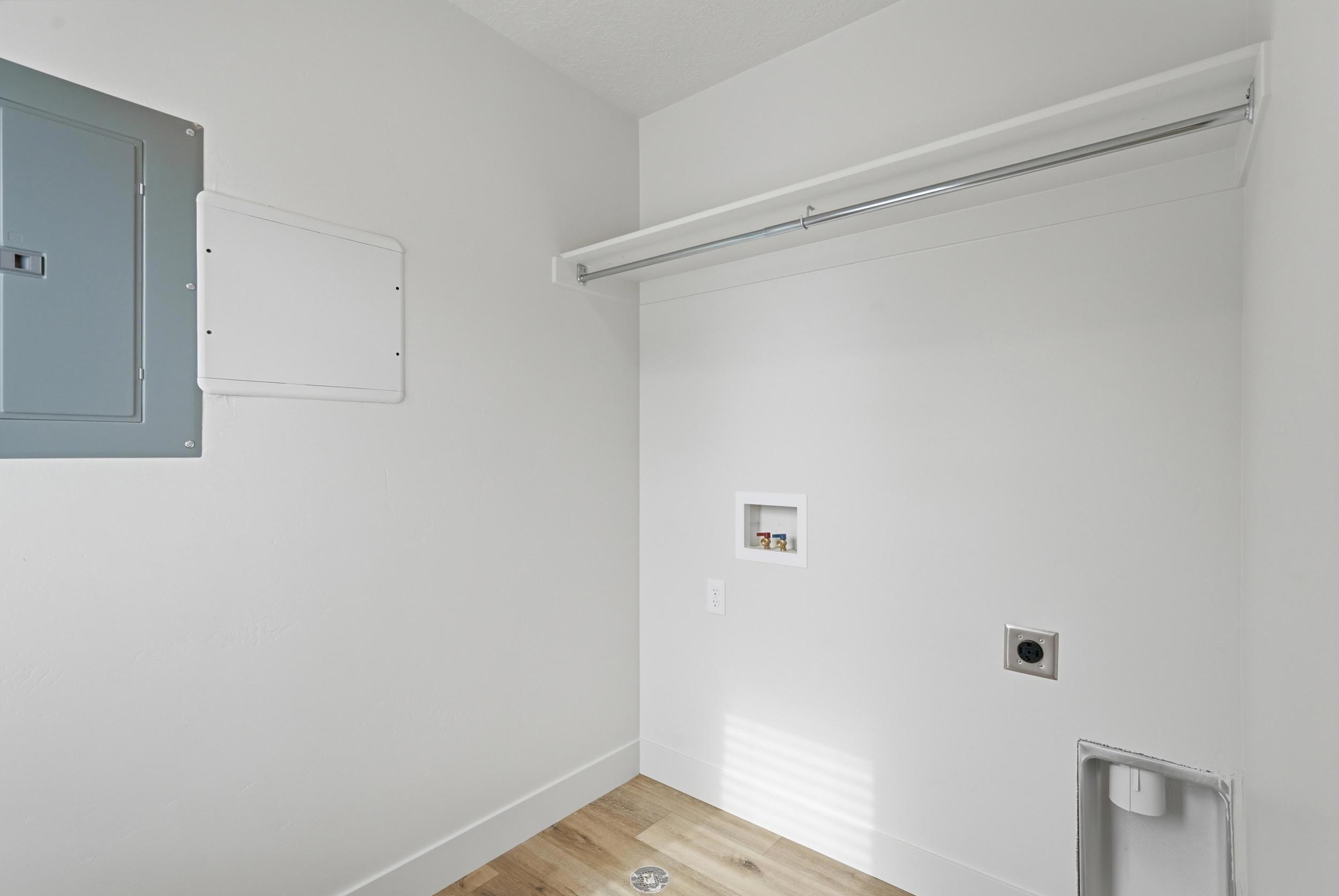 Dedicated laundry area featuring light wood-finish flooring, white baseboards, and bright white walls