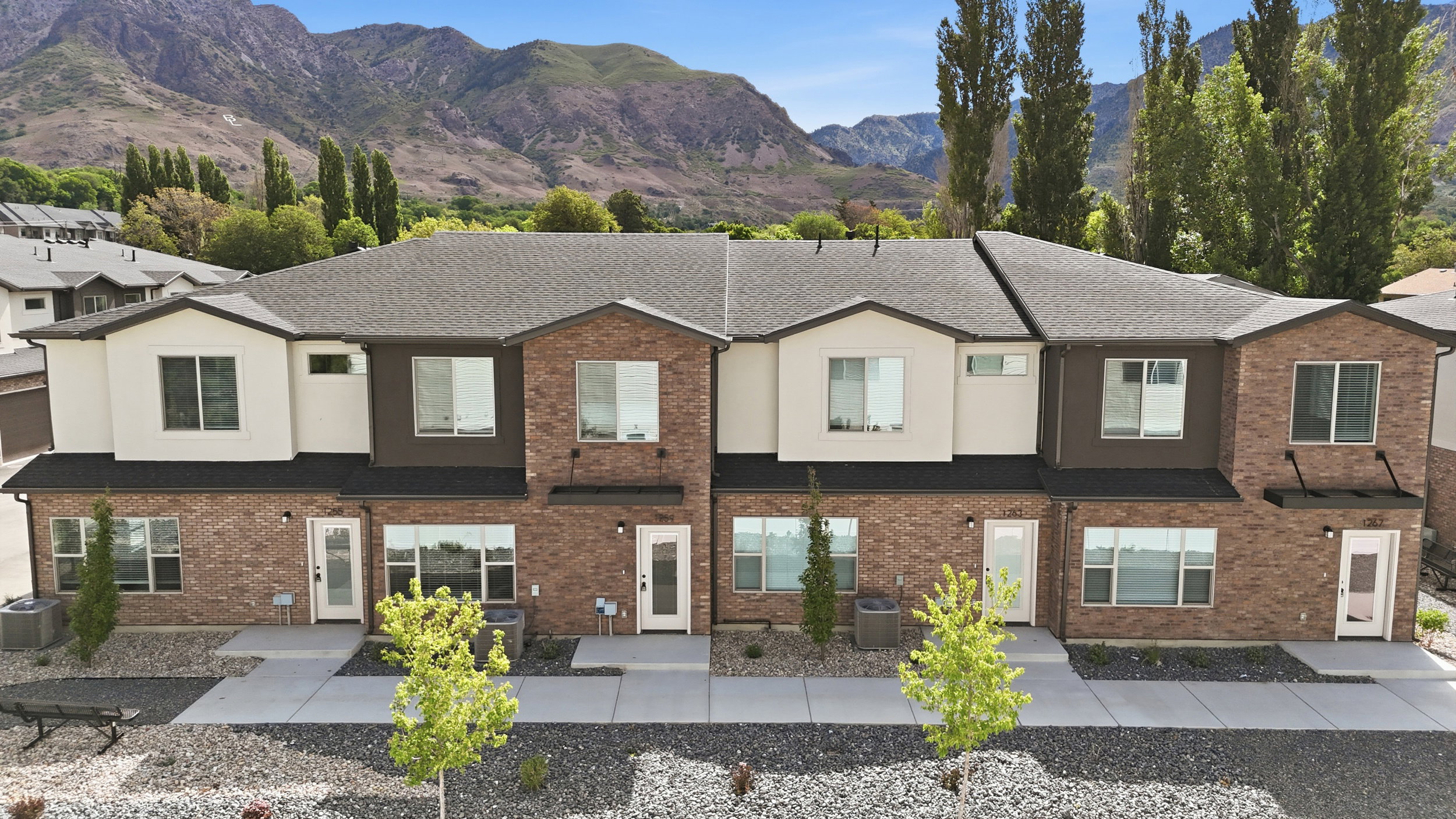 Contemporary townhome exteriors featuring brick and stucco finishes, multiple large windows for abundant natural light, and a dark shingle roof