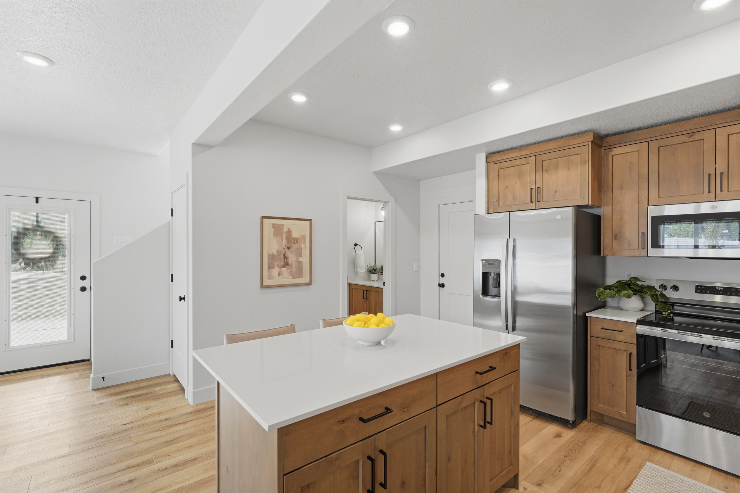 Open-concept kitchen featuring a central island with a white countertop, wood-finish cabinetry, stainless steel appliances, and recessed lighting