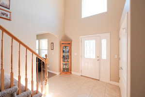 Foyer featuring a tall ceiling, decorative glass front door, matching sidelight, tiled flooring, and a natural wood staircase with carpeted treads