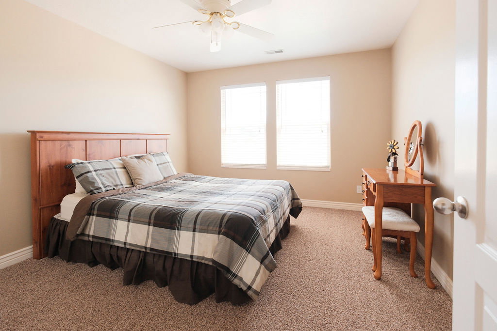 Neutral-toned bedroom featuring two windows, light tan walls, and textured carpeting