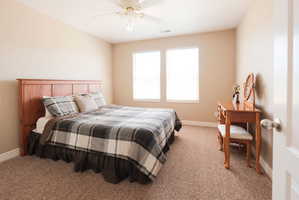 Neutral-toned bedroom featuring two windows, light tan walls, and textured carpeting