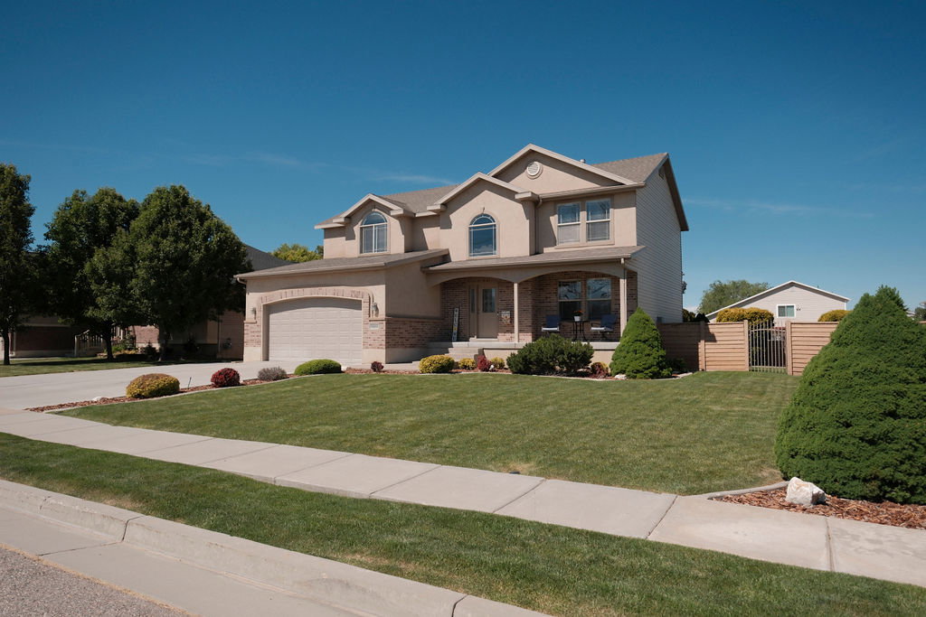 Two-story property featuring a stucco and brick exterior, an arched entryway, a covered porch, a two-car garage, and a manicured front lawn