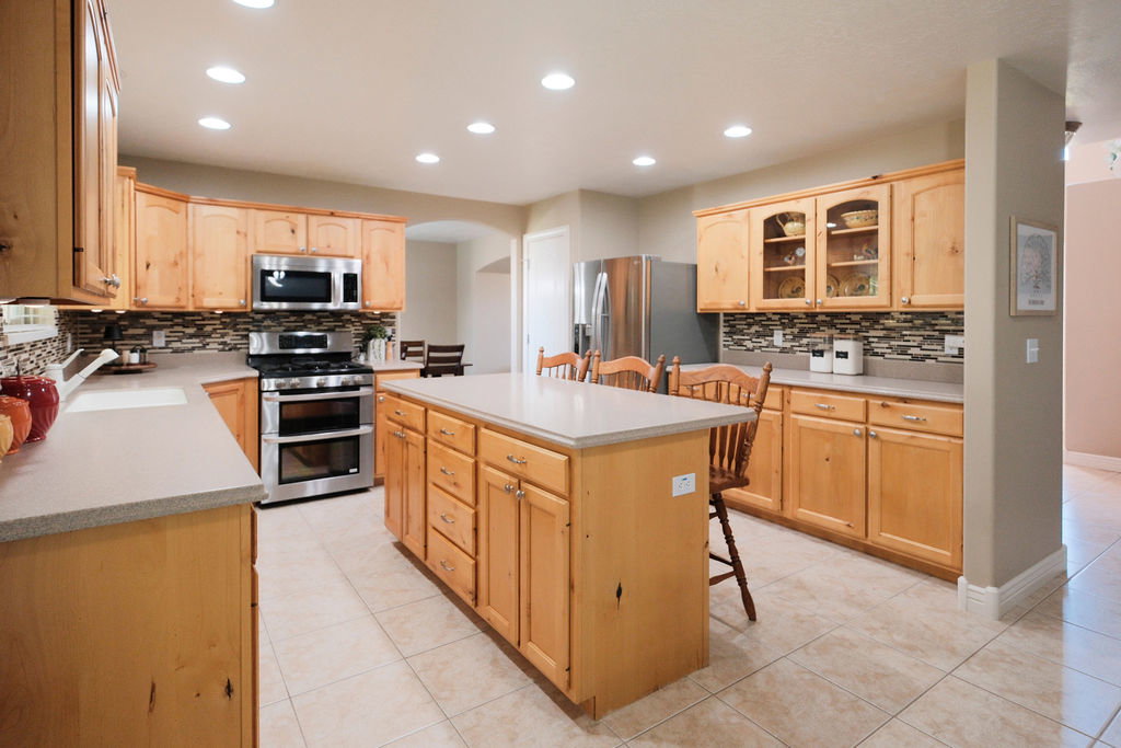 Spacious kitchen featuring light wood cabinetry, a large central island, stainless steel appliances, tile flooring, and recessed lighting