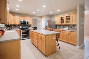 Spacious kitchen featuring light wood cabinetry, a large central island, stainless steel appliances, tile flooring, and recessed lighting