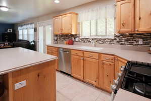 Kitchen featuring wood cabinetry, a mosaic tile backsplash, a stainless steel dishwasher, an integrated sink, and light-toned countertops