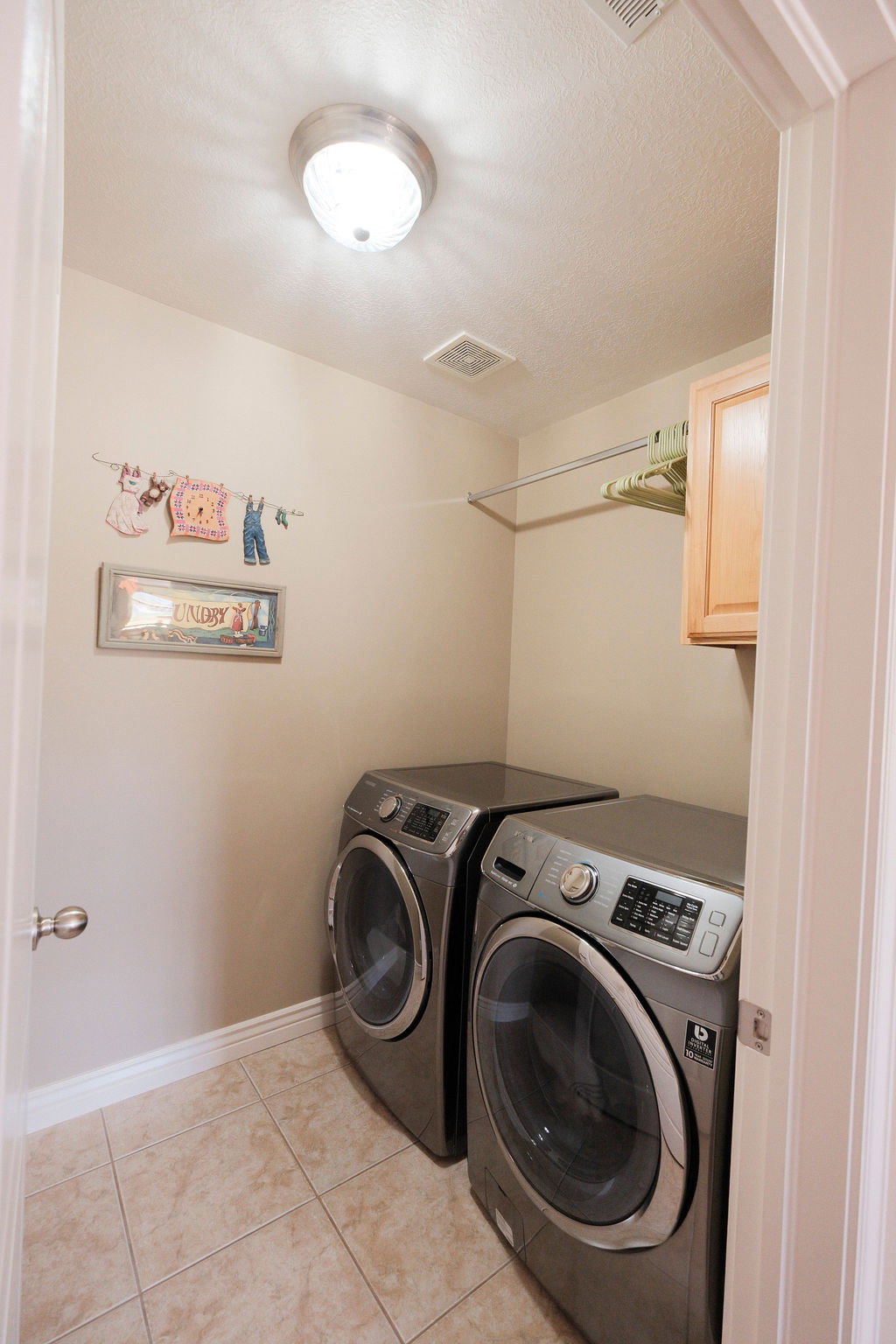 Dedicated laundry area featuring ceramic tile flooring, a wall-mounted drying rod, and a built-in upper cabinet