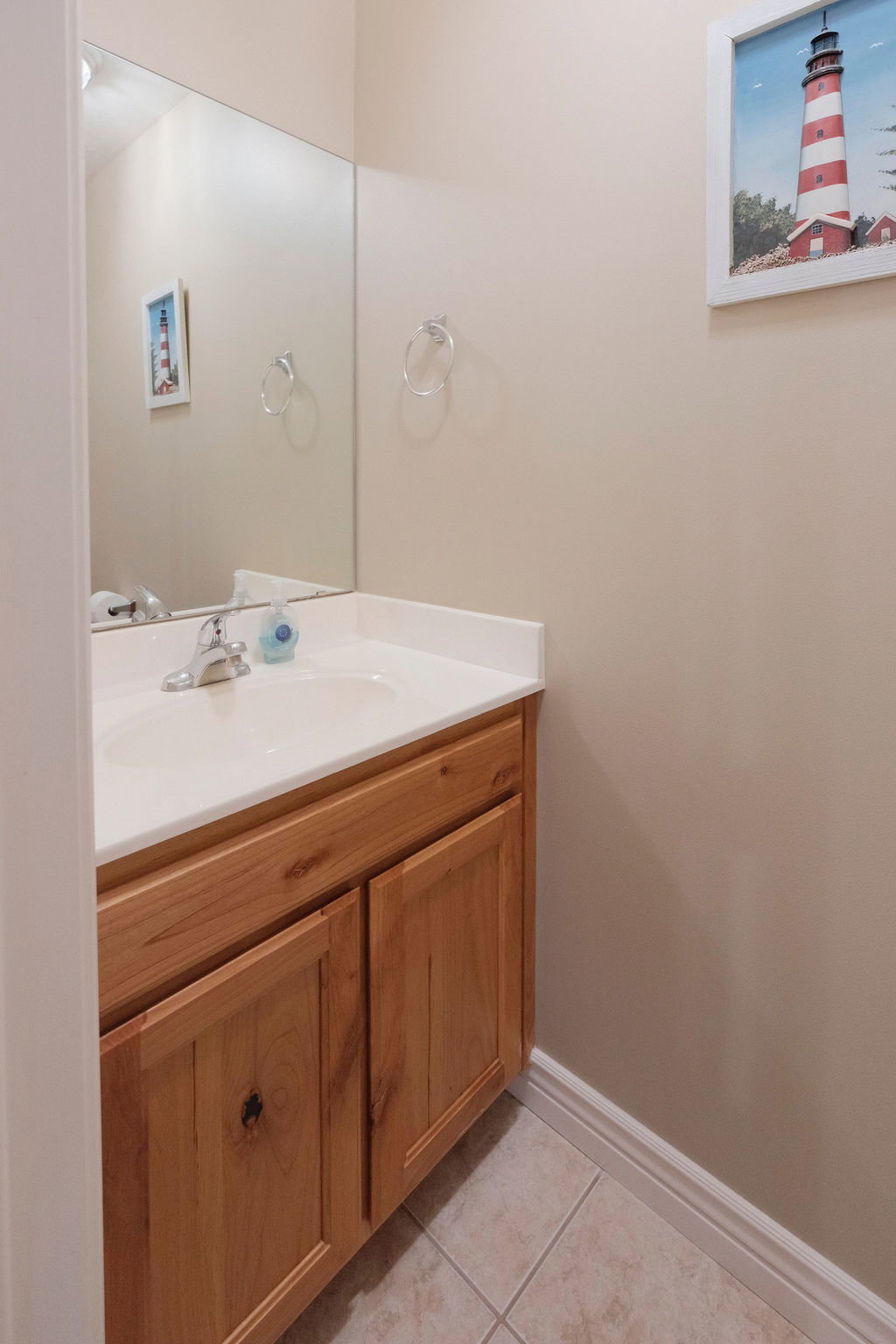 Powder room featuring a wood-finish vanity with panel doors, an integrated sink, a large wall mirror, and tile flooring