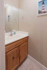 Powder room featuring a wood-finish vanity with panel doors, an integrated sink, a large wall mirror, and tile flooring