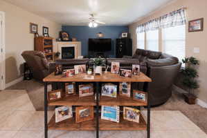 Living area featuring a fireplace with a light-colored mantel, three windows, and a ceiling fan
